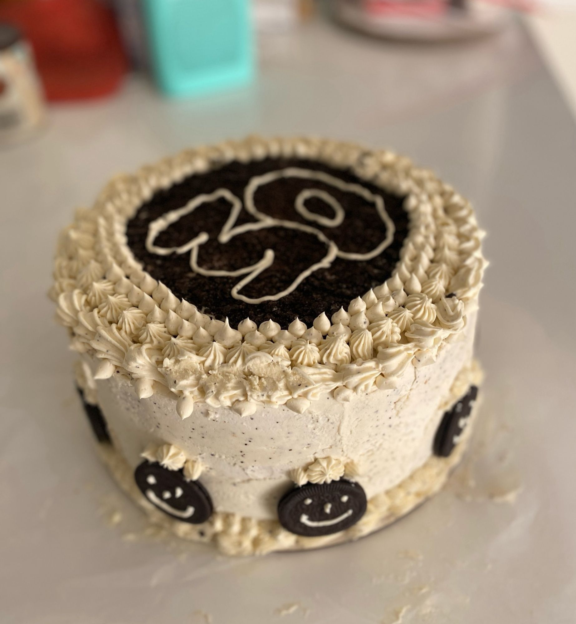 White frosted birthday cake with Oreos on the side (they have little smiley faces on them) and the number “30” piped on top with white frosting on an Oreo crumb background