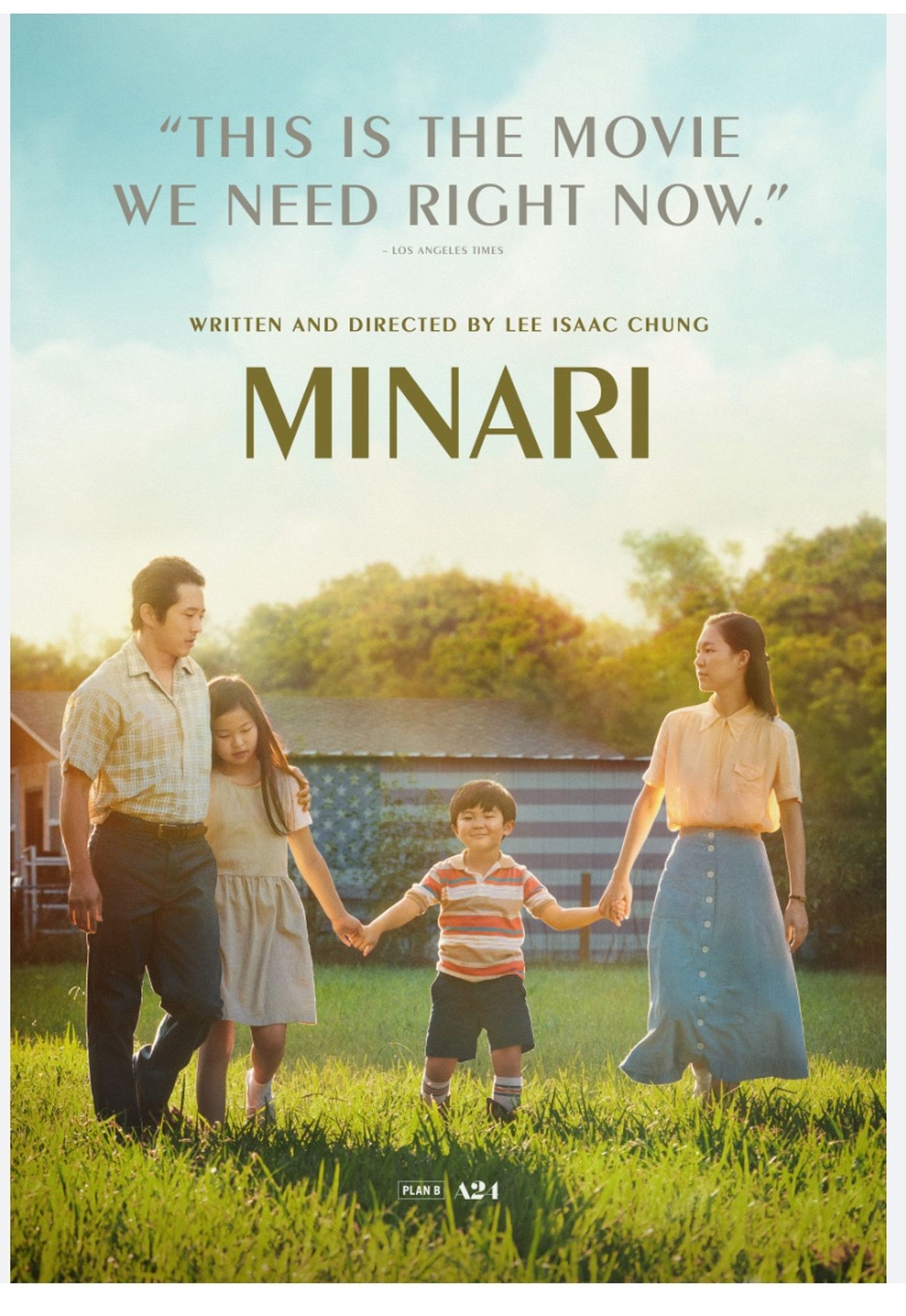 Minari. The picture shows a young Korean family, parents and son and daughter, holding hands in a grassy field in the US. There’s a large barn in the background.