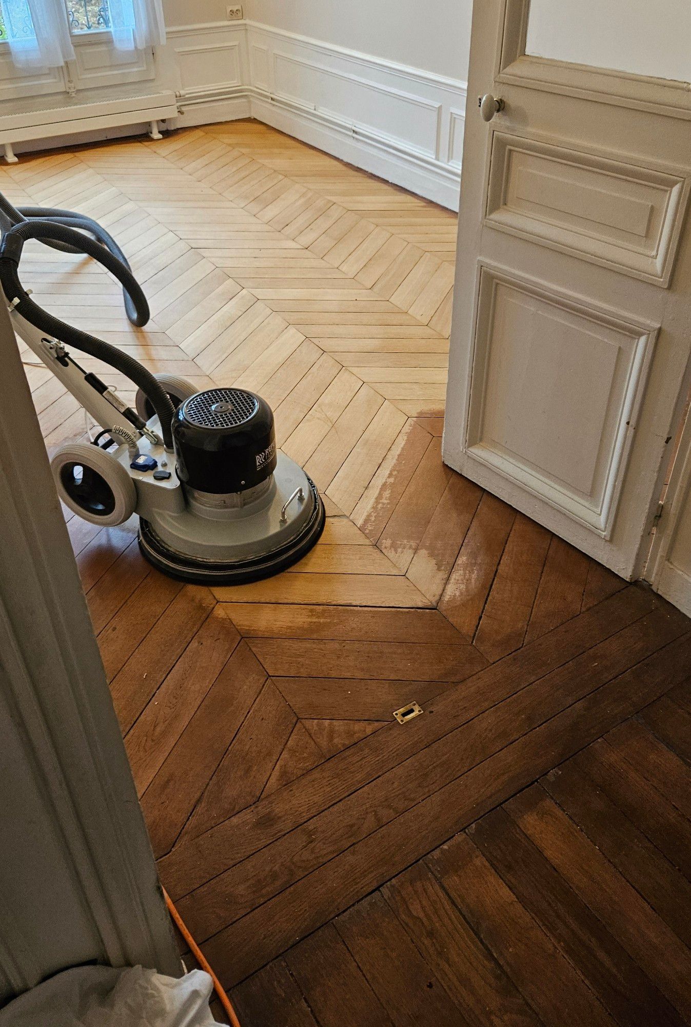 Une ponçeuse passe sur un vieux parquet usé, lui rendant son éclat d'antan