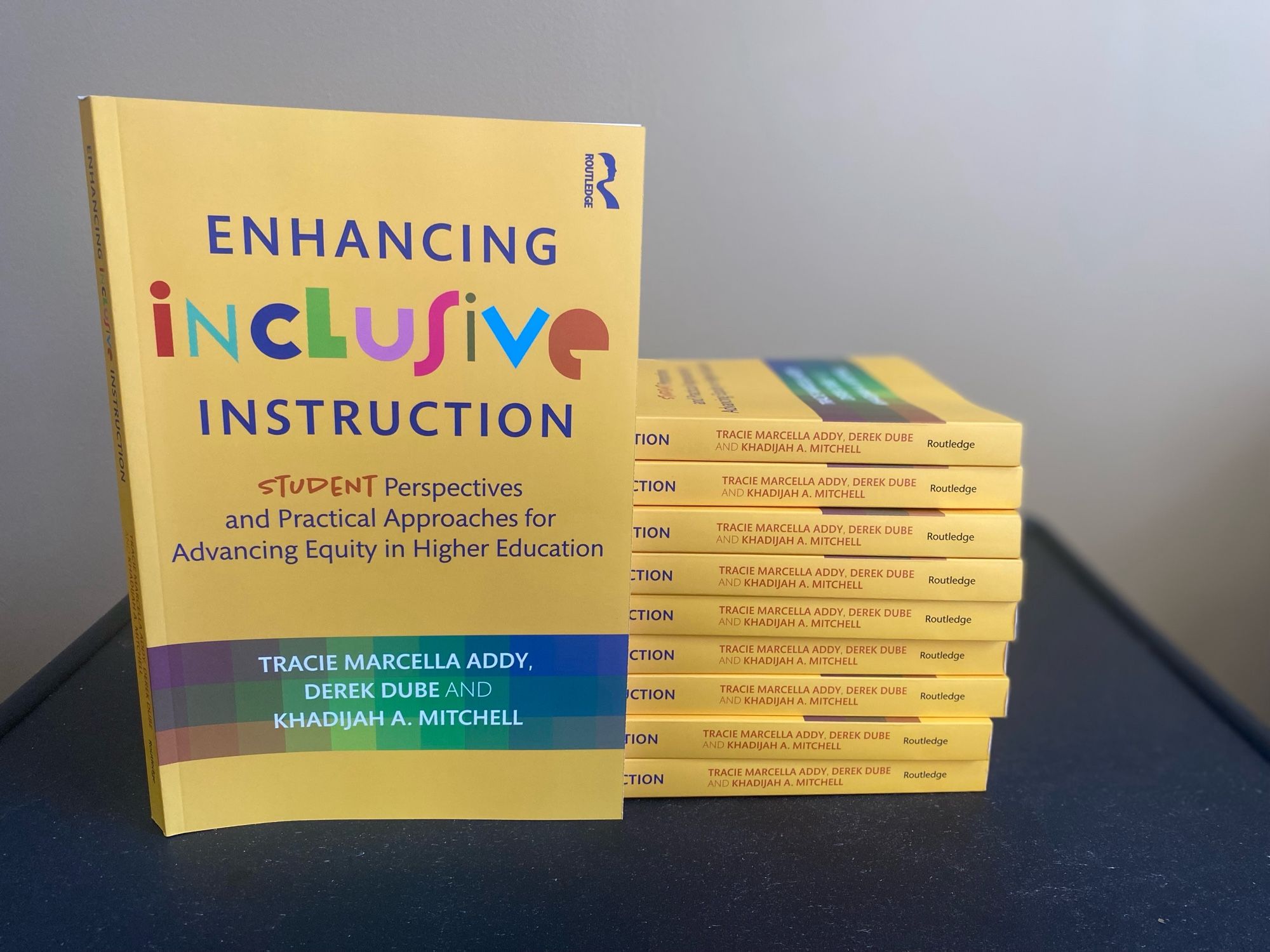 Several copies of the book Enhancing Inclusive Instruction. One upright and several stacked.