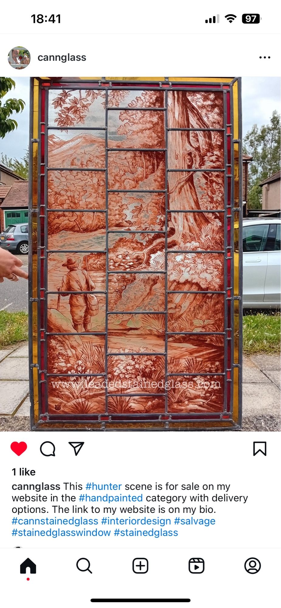 Instagram post from cannglass with a photo of an intricately painted stained glass window panel featuring a man in a woodland scene, brown in colour, with red and yellow borders.