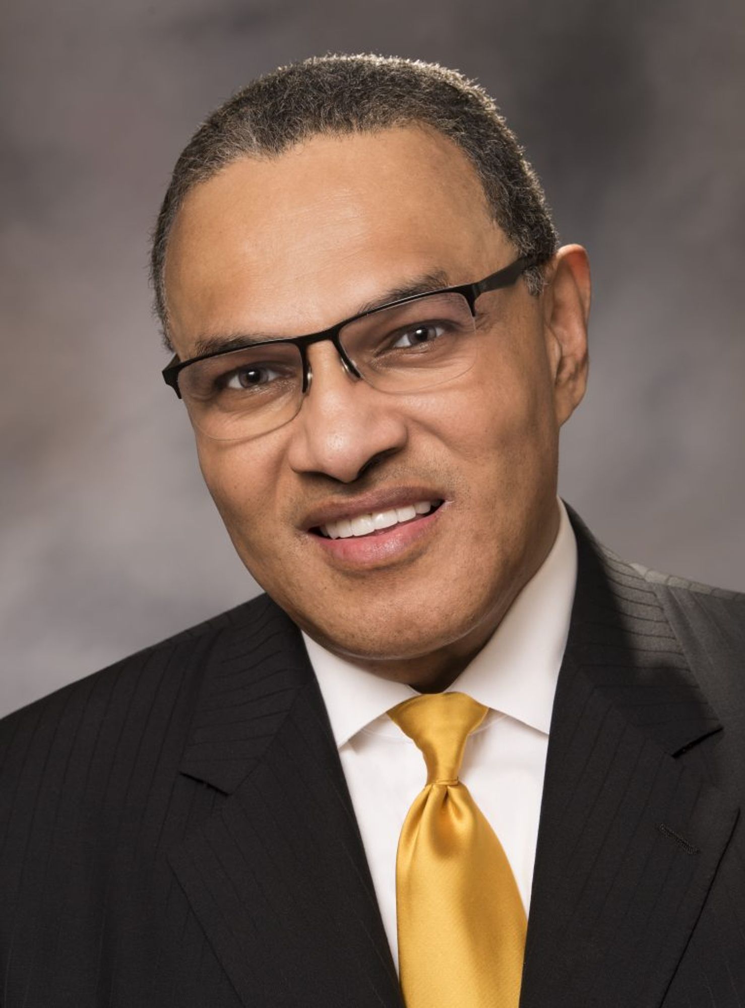 Image of a man with glasses , a suit and gold tie