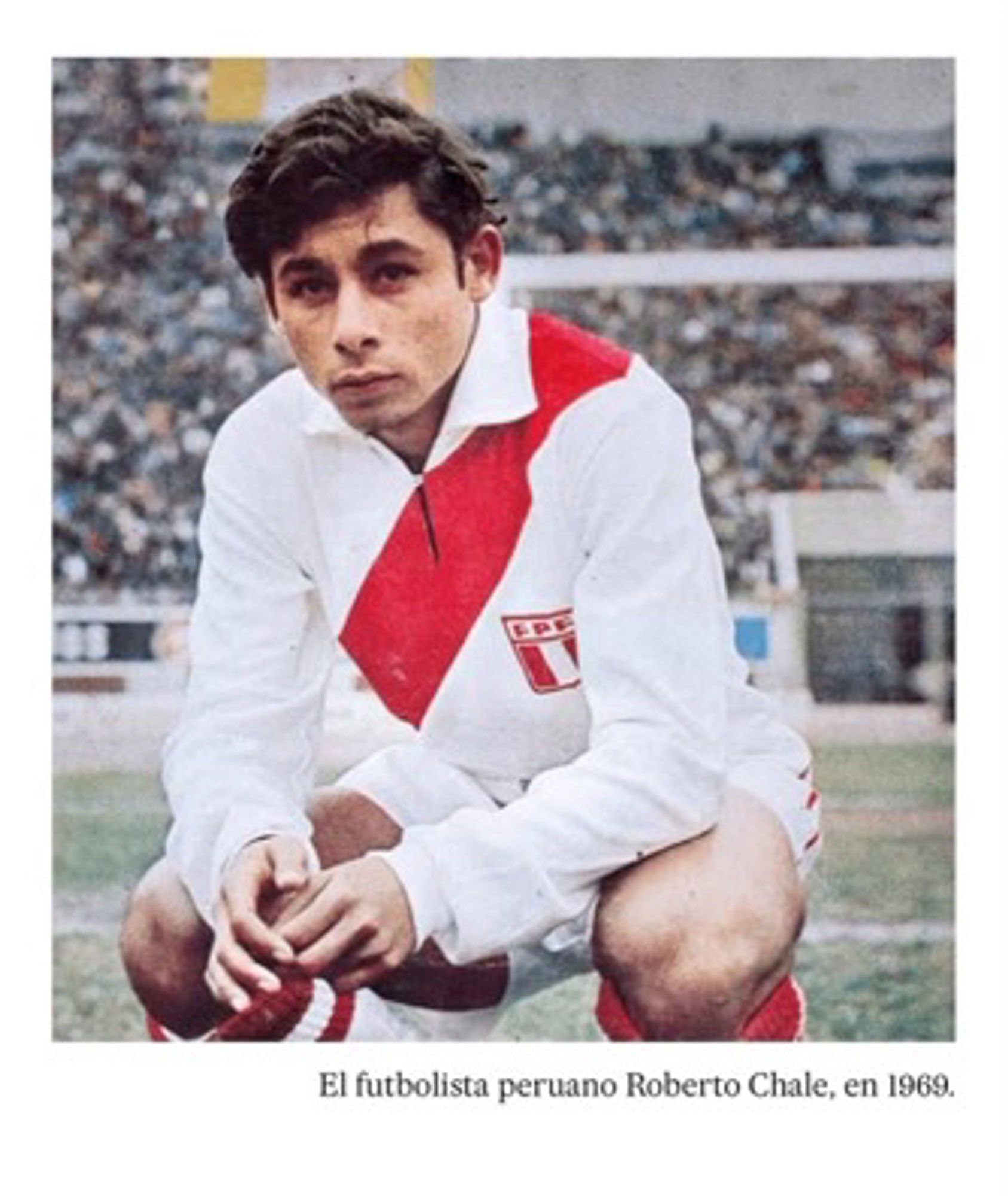 Pregame portrait of Peru and Universitario de Deportes legend Roberto Chale. The picture is from the 1969. He is crouched and looking at the camera at a slight angle. He is wearing a long sleeve Peru shirt with the iconic red sash running from left shoulder to right hip. It has a large floppy collar and a deep slit that clips shut at the neck. He is elegant and beautiful