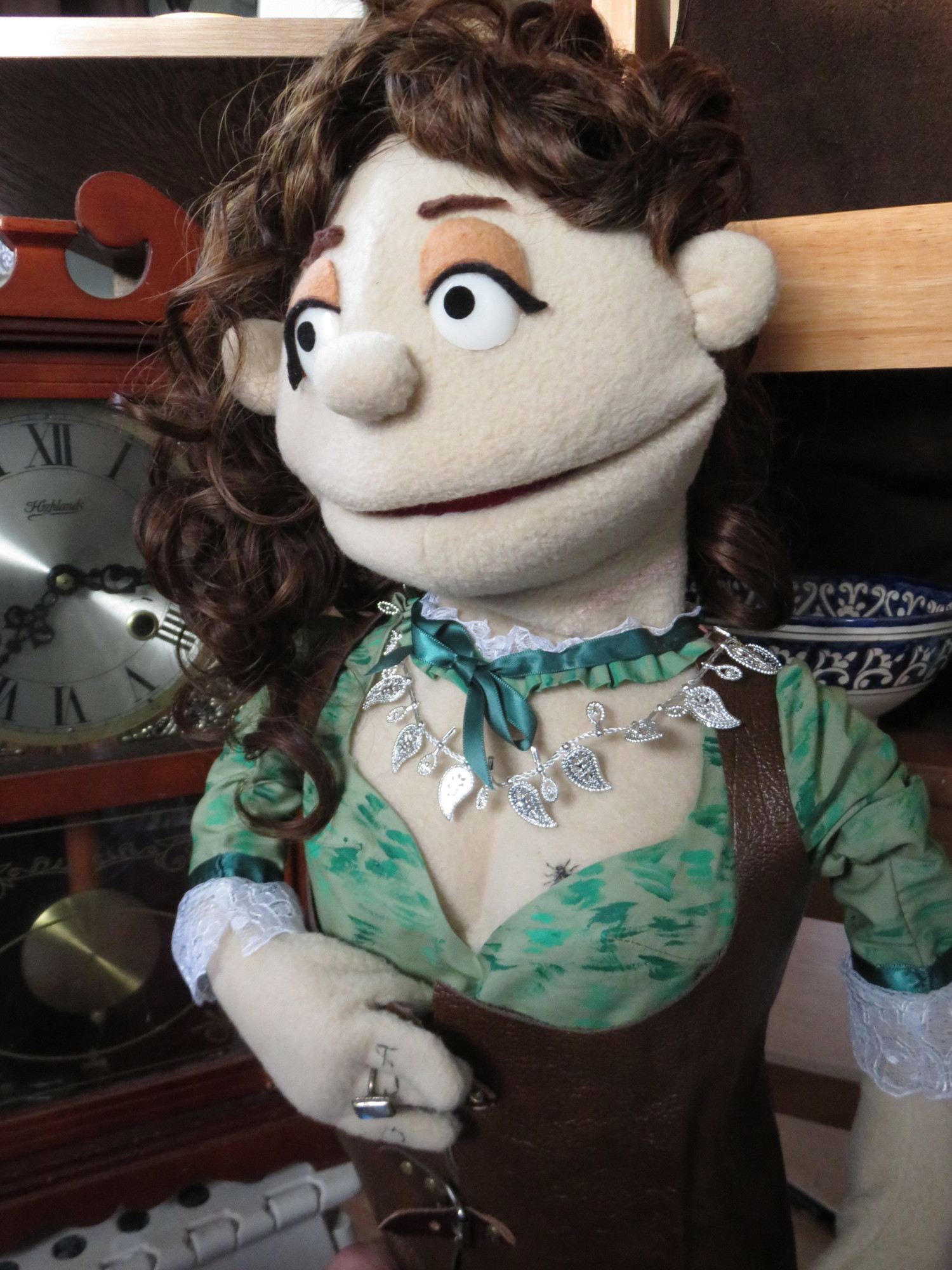 Three images of a muppet of Anne Bonny from Our Flag Means Death in front of an old clock and some ornaments and dishes on a shelf