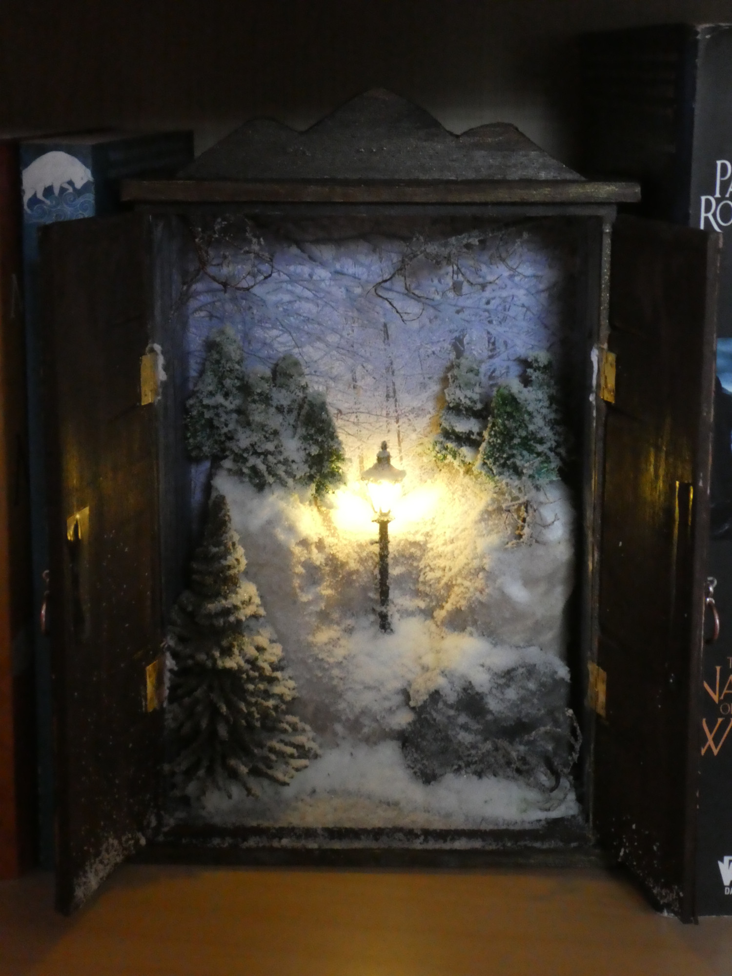 A miniature book nook with a snowy scene from the Lion the Witch and the Wardrobe inside, with an illuminated lamppose