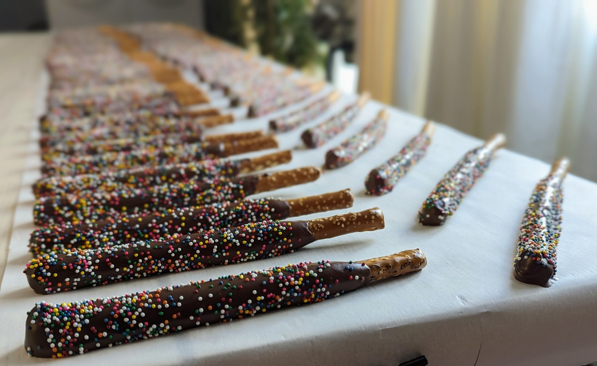 A portrait photo of dozens of decorated pretzel rods. The pretzels are covered in chocolate with rainbow nonpareils.