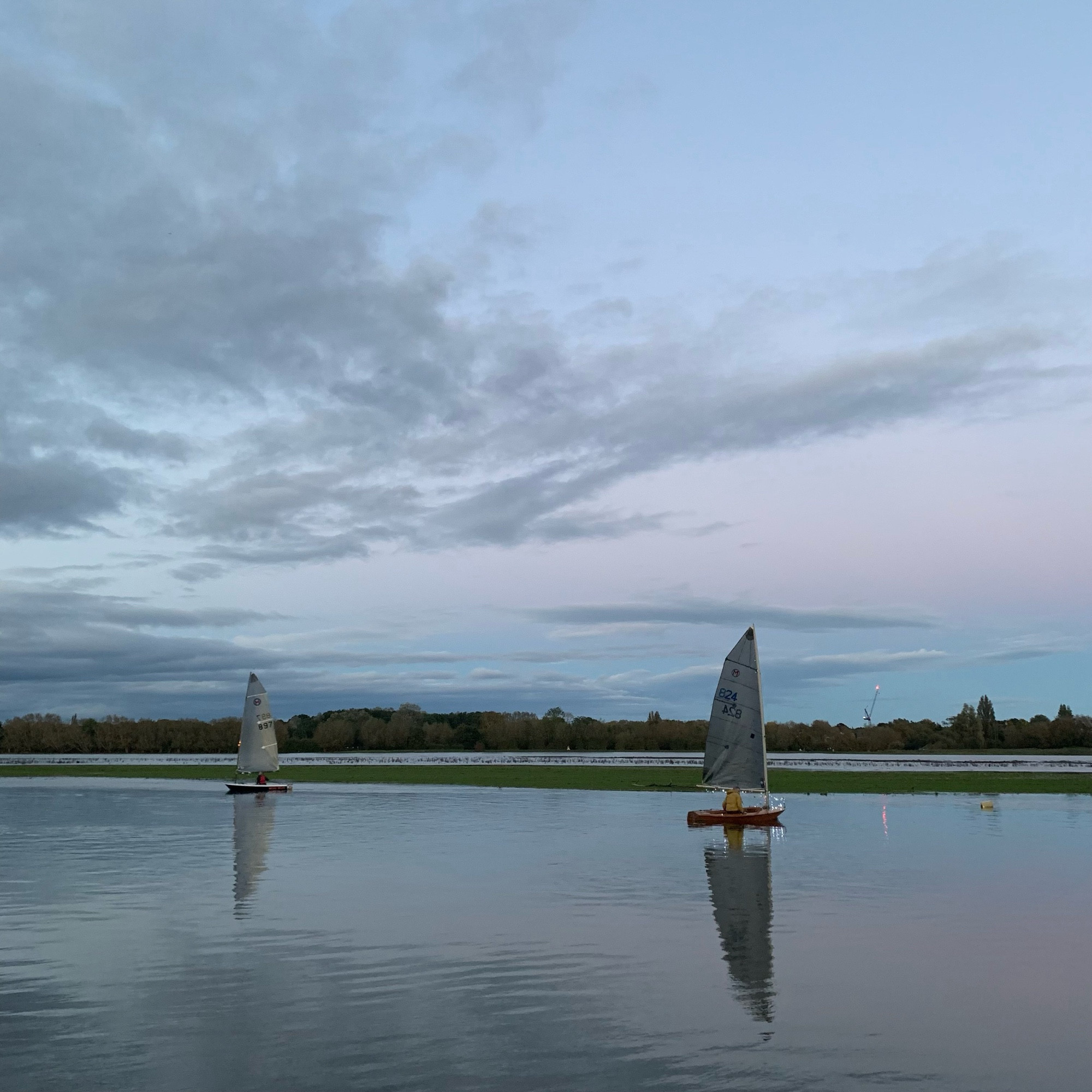 Two Mirror dinghies on the river Thames at dusk. Fairy lights are visible on one.