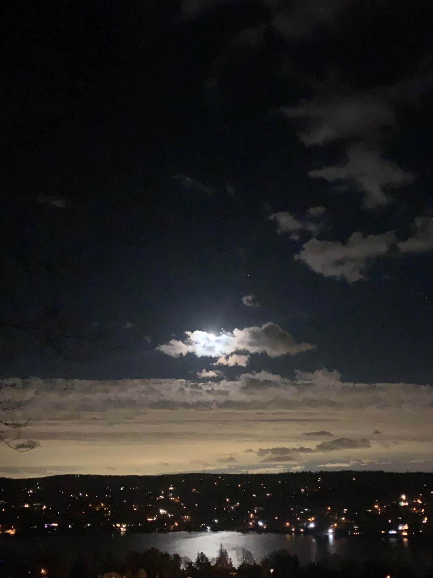 The moon above after a storm passes, just breaking through; the clouds now east reflecting urban light.