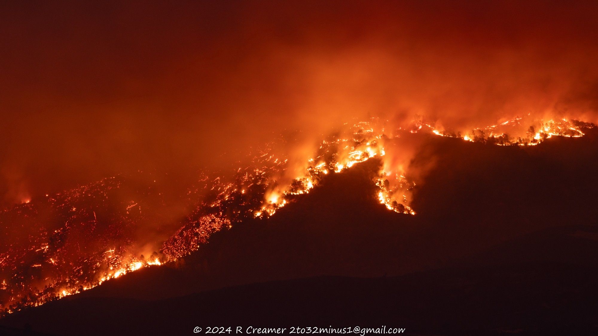 A sierra foothills mountain burning at night showing tall flames amid trees and brush