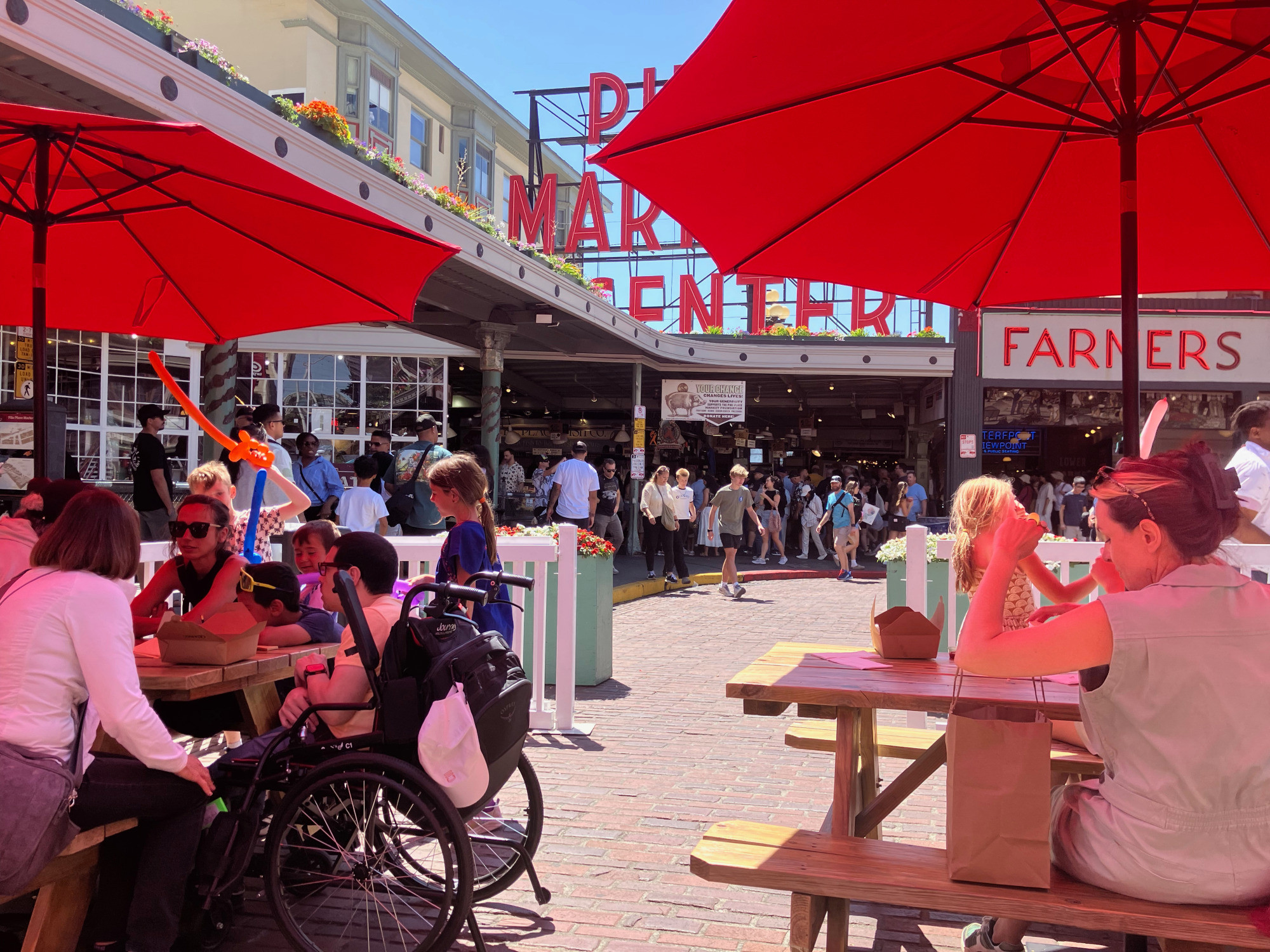people sitting at tables in street on benches and in wheelchairs