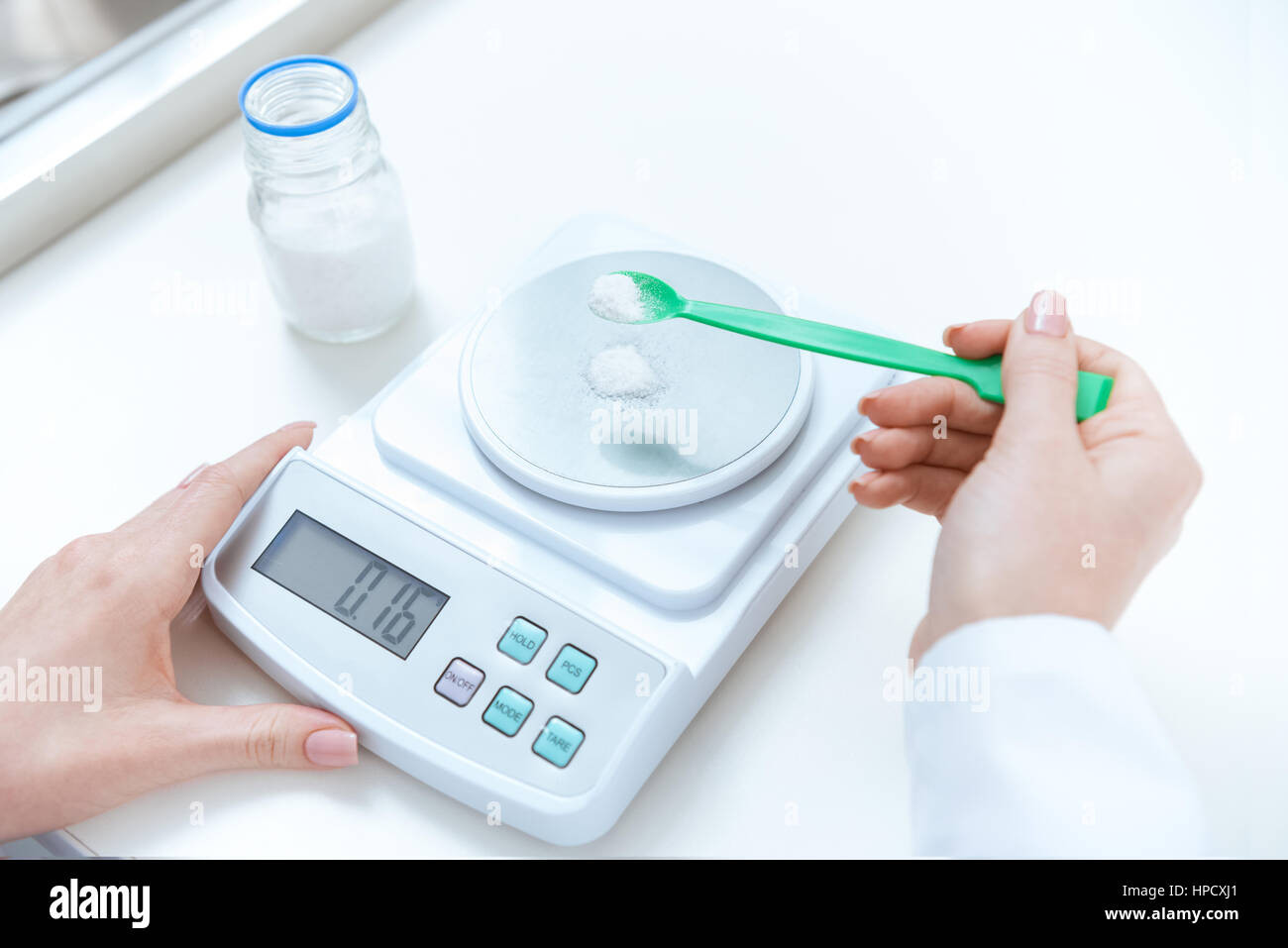 An alamy stock photo of someone measuring white powder directly on a digital scale.