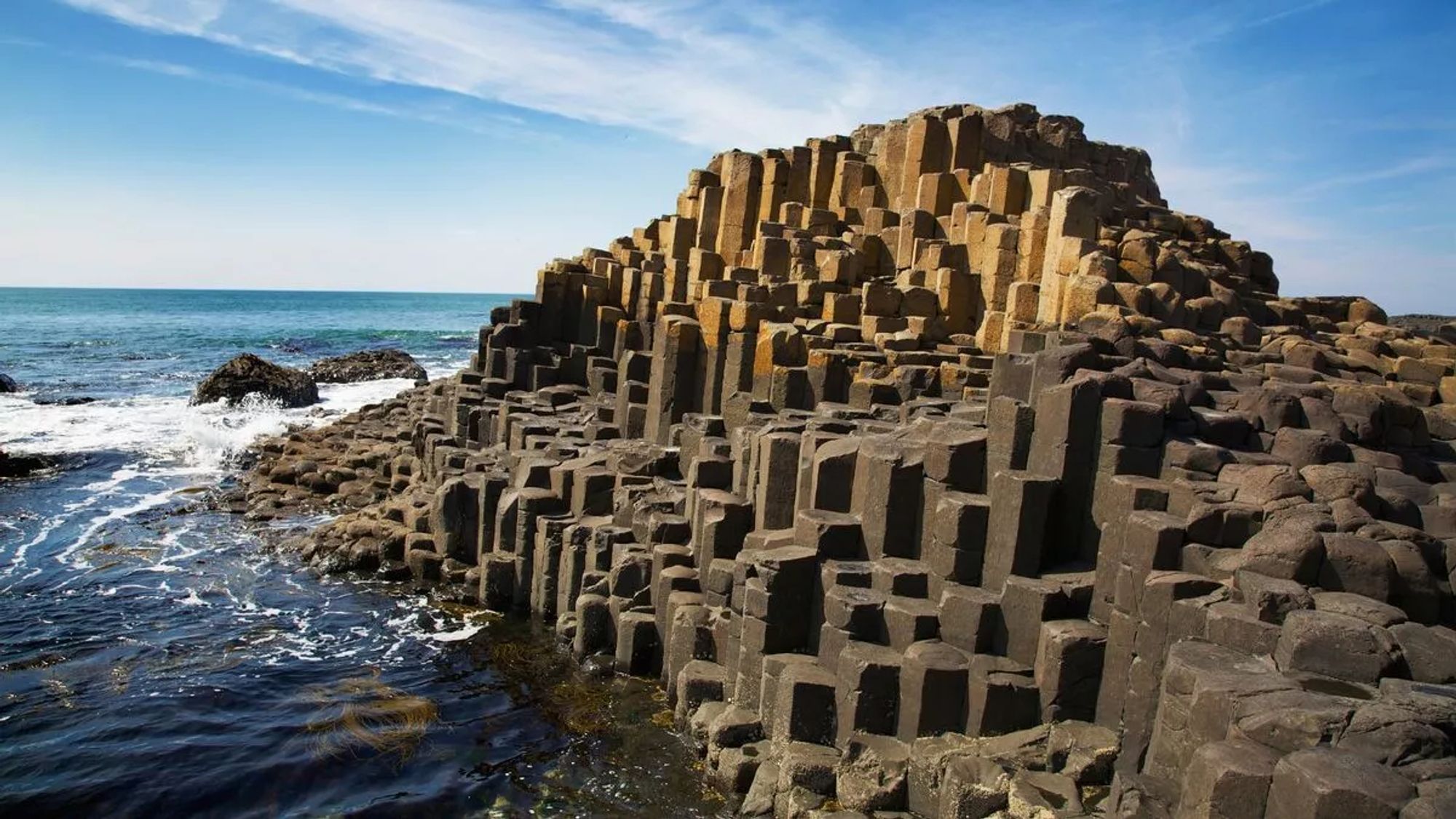 A seaside rock formation appears to be made of roughly hexagonal columns arranged vertically, packed together like crayons in a pack.  A blue sky and ocean foam is visible behind the rock formation.

"The Giant's Causeway in Northern Ireland has been around for millions of years, but it seems that recently the landmark has enjoyed a surge in popularity.
The unusual rock formation often tops the list of best things to see in Northern Ireland, and it's previously won accolades such as the Best UK Heritage attraction in 2017."
https://www.mirror.co.uk/travel/uk-ireland/giants-causeway-facts-northern-ireland-11613873