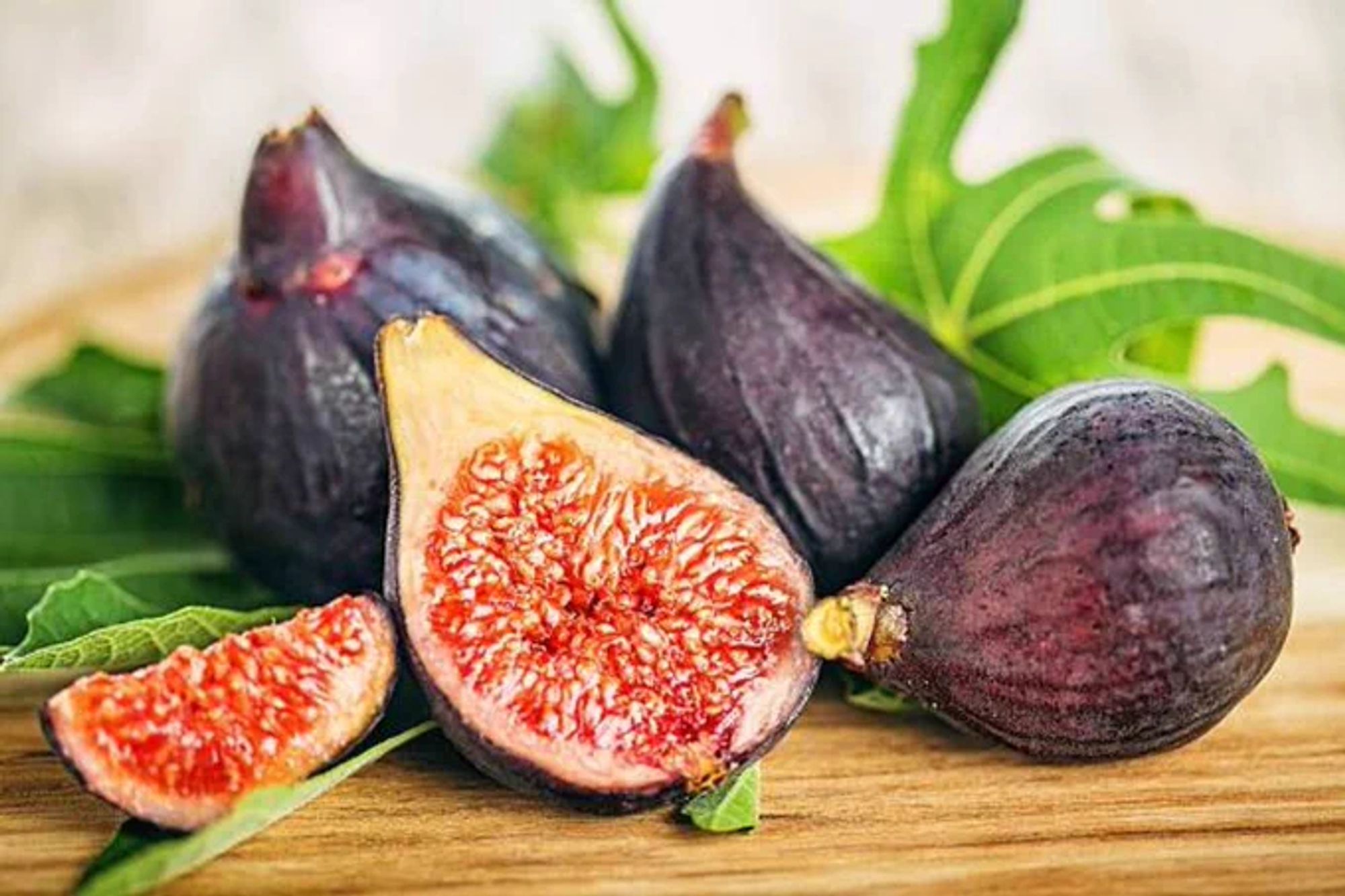 Stock photo of some figs on a cutting board with fig leaves behind them.