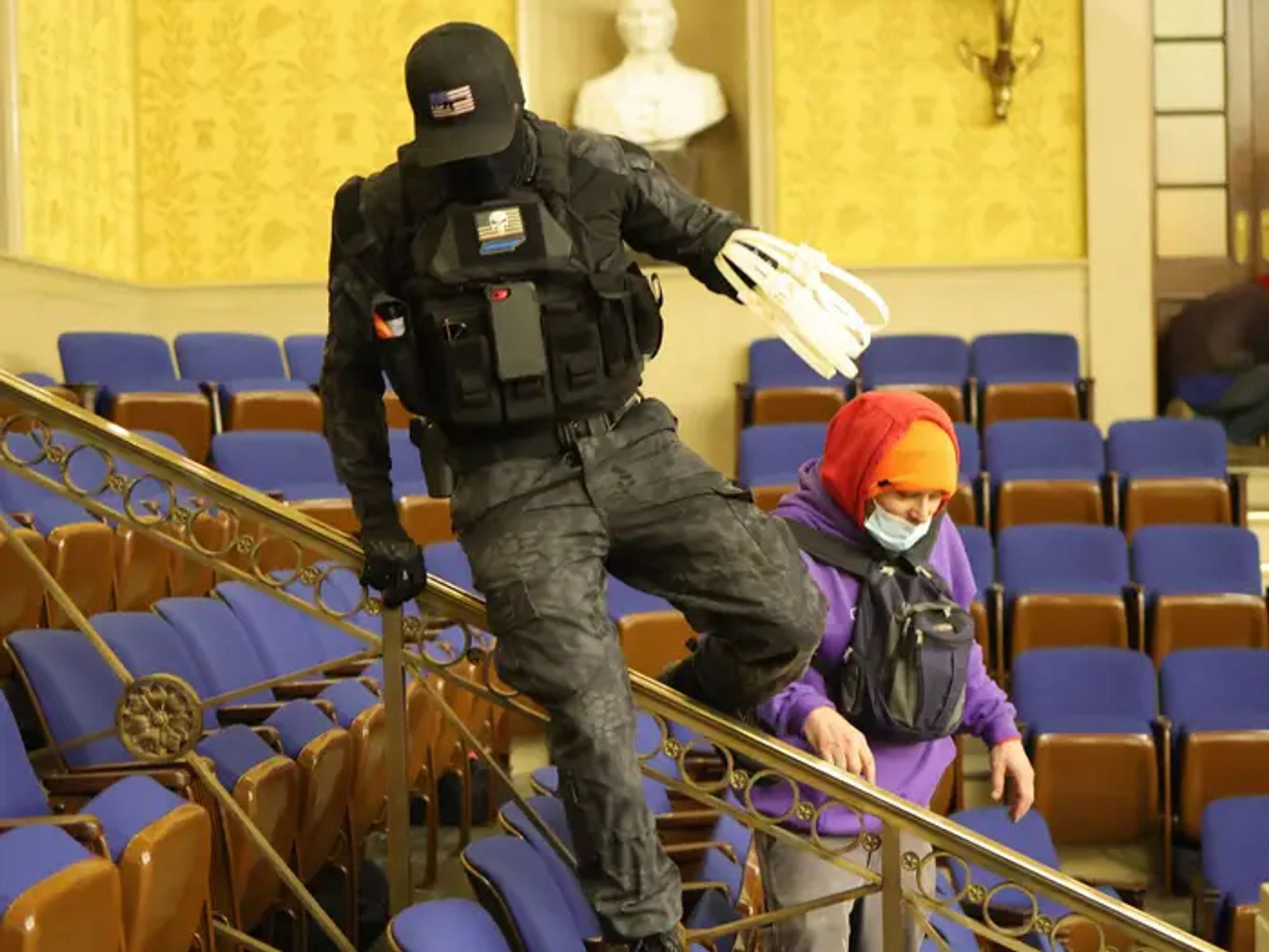 The Jan 6th rioter in black and light body armor carries a stack of zip-tie handcuffs for restraining people.