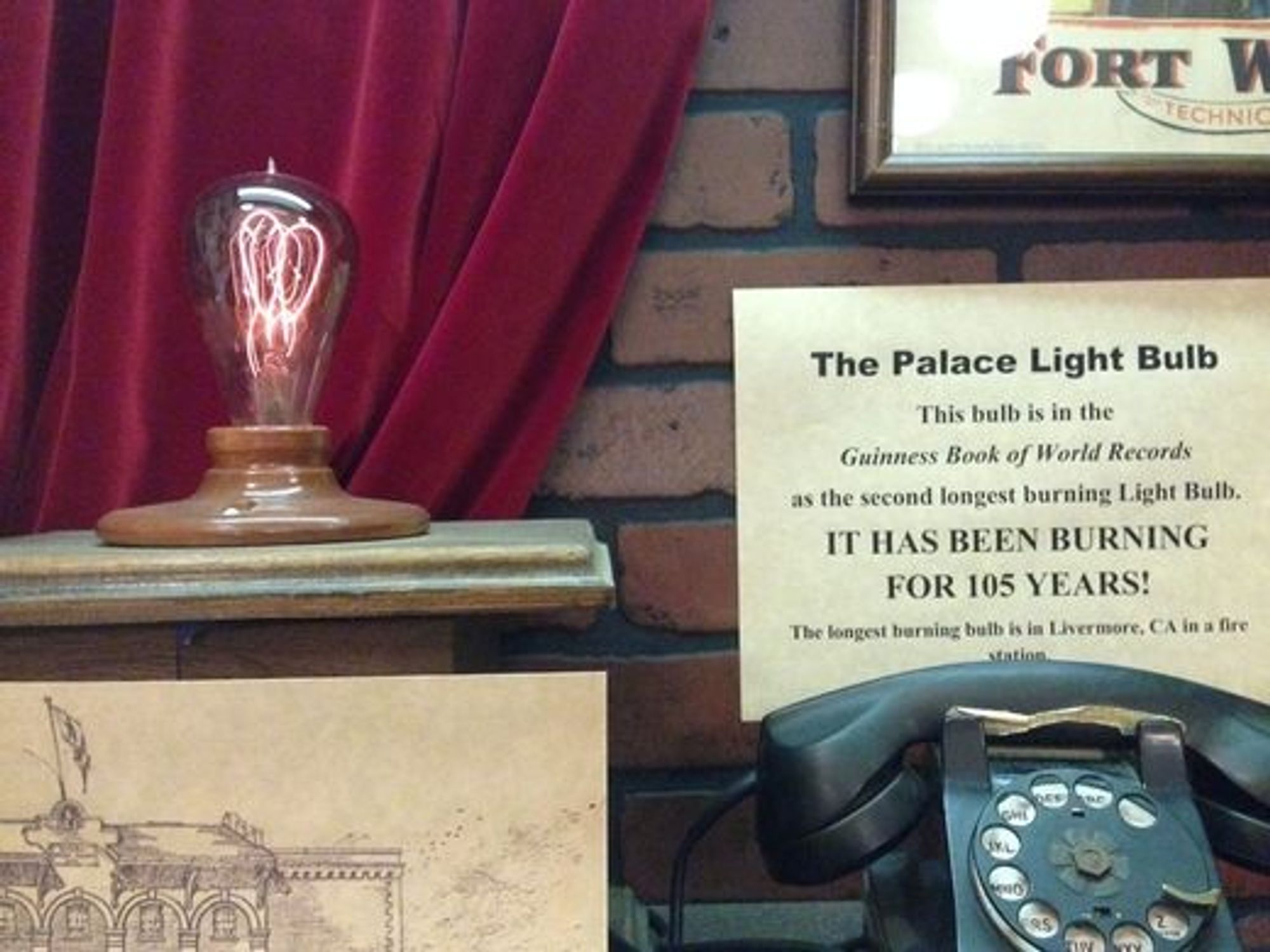 The Palace Light Bulb exhibit has been relocated to the Forth Worth Stockyards, where it's present in a display.  The bulb is kept on a low-voltage circuit.

I saw it in 2021 (?), hopefully it hasn't burned out since then : (

https://www.atlasobscura.com/places/the-palace-light-bulb-fort-worth-texas