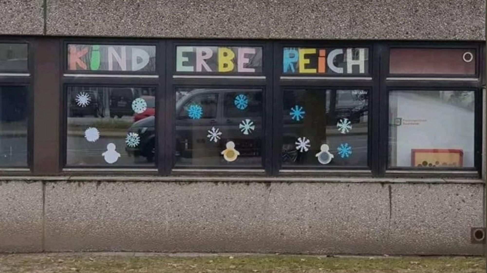 Eine Waschbetonfassade mit mehreren Fenstern. Auf dreien davon steht- weil der Platz pro Fenster begrenzt ist - „KIND“ „ERBE“ REICH“