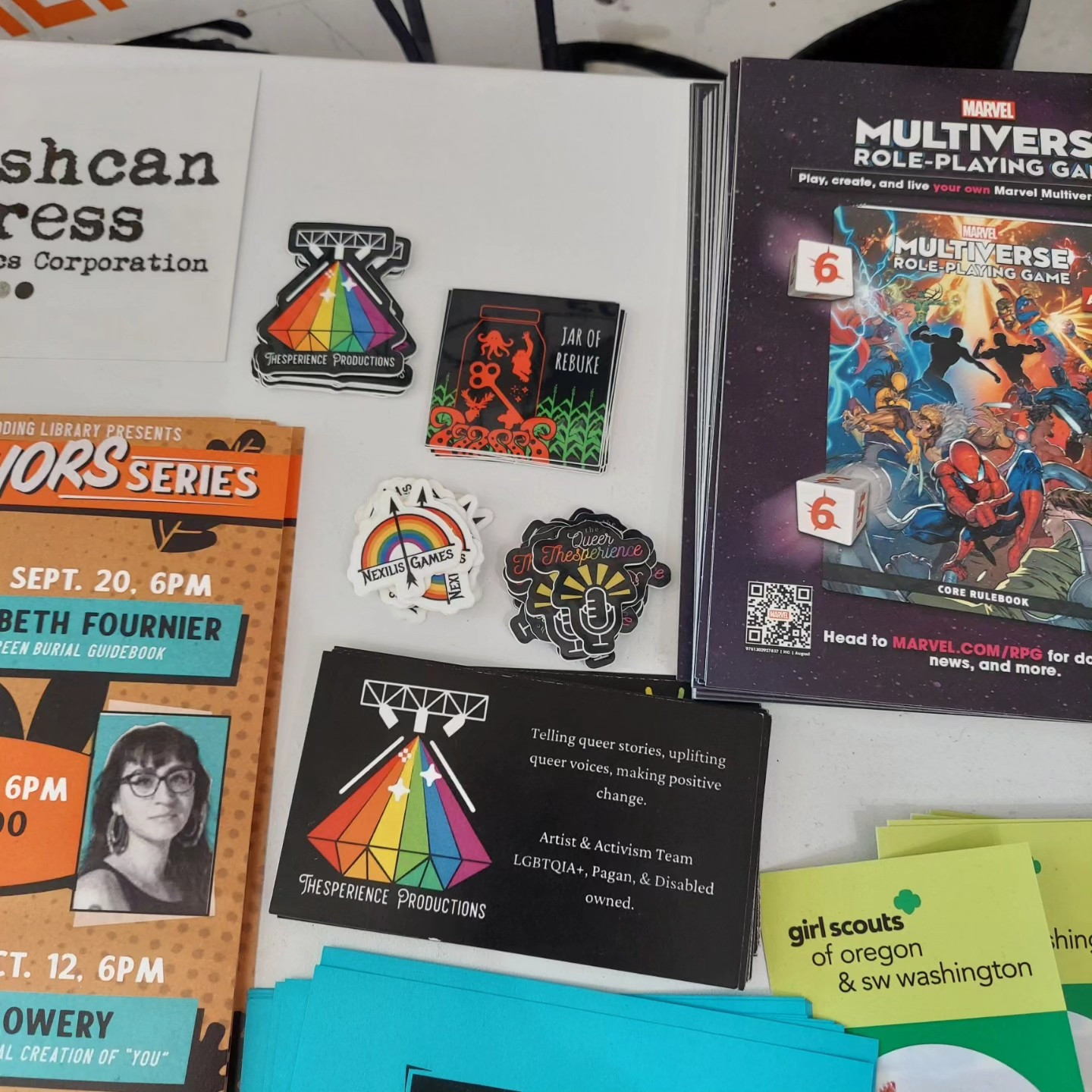 A collection of Thesperience business cards and small stickers of the Nexilis Games, Jar of Rebuke, The Queer Thesperience, and of the Thesperience logo!   These items are surrounded by other flyers.