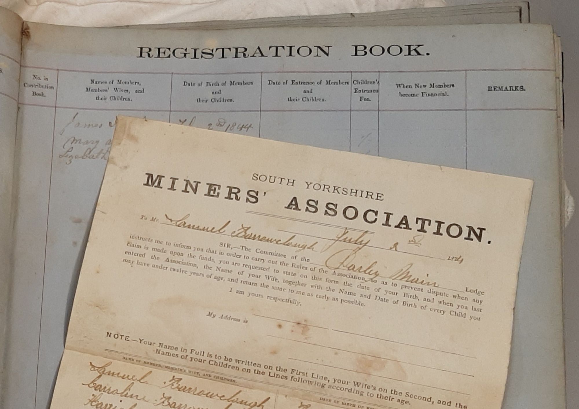 Open page of a registration book recording members of a South Yorkshire Miners' Association Lodge. A form submitted by a member is lying across the page.