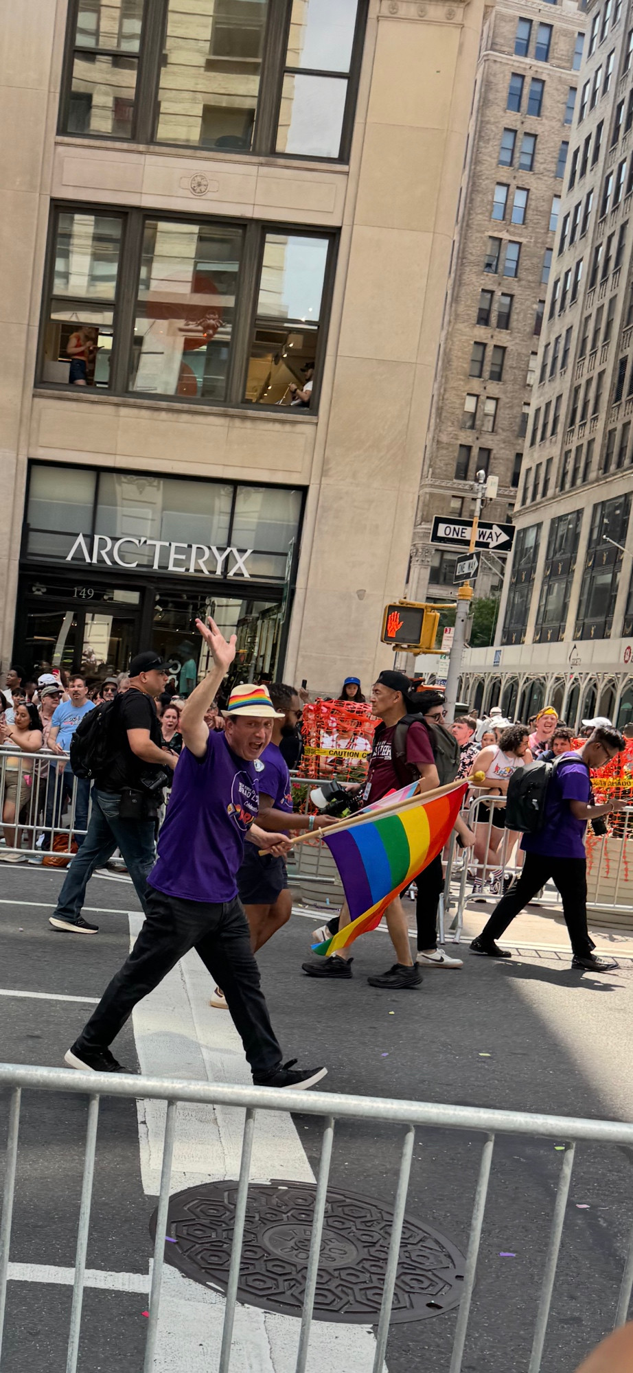 Brad Lander walks in the NYC Pride March with a big rainbow flag, a rainbow straw hat, and a giant happy grin