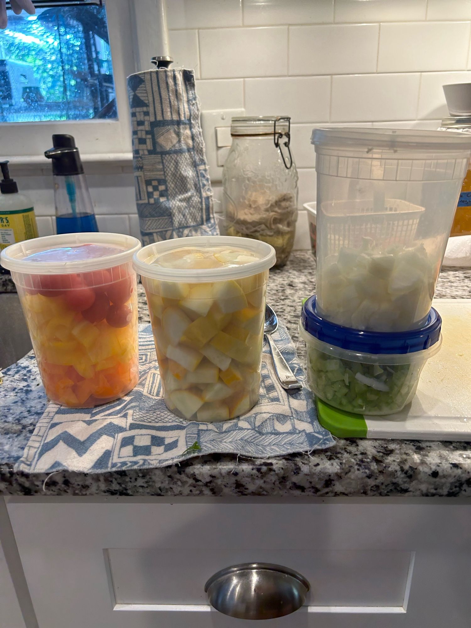 4 deli containers of produce. The left is bell peppers, the center is squash. The right has a stacked onion container on a celery and onion container