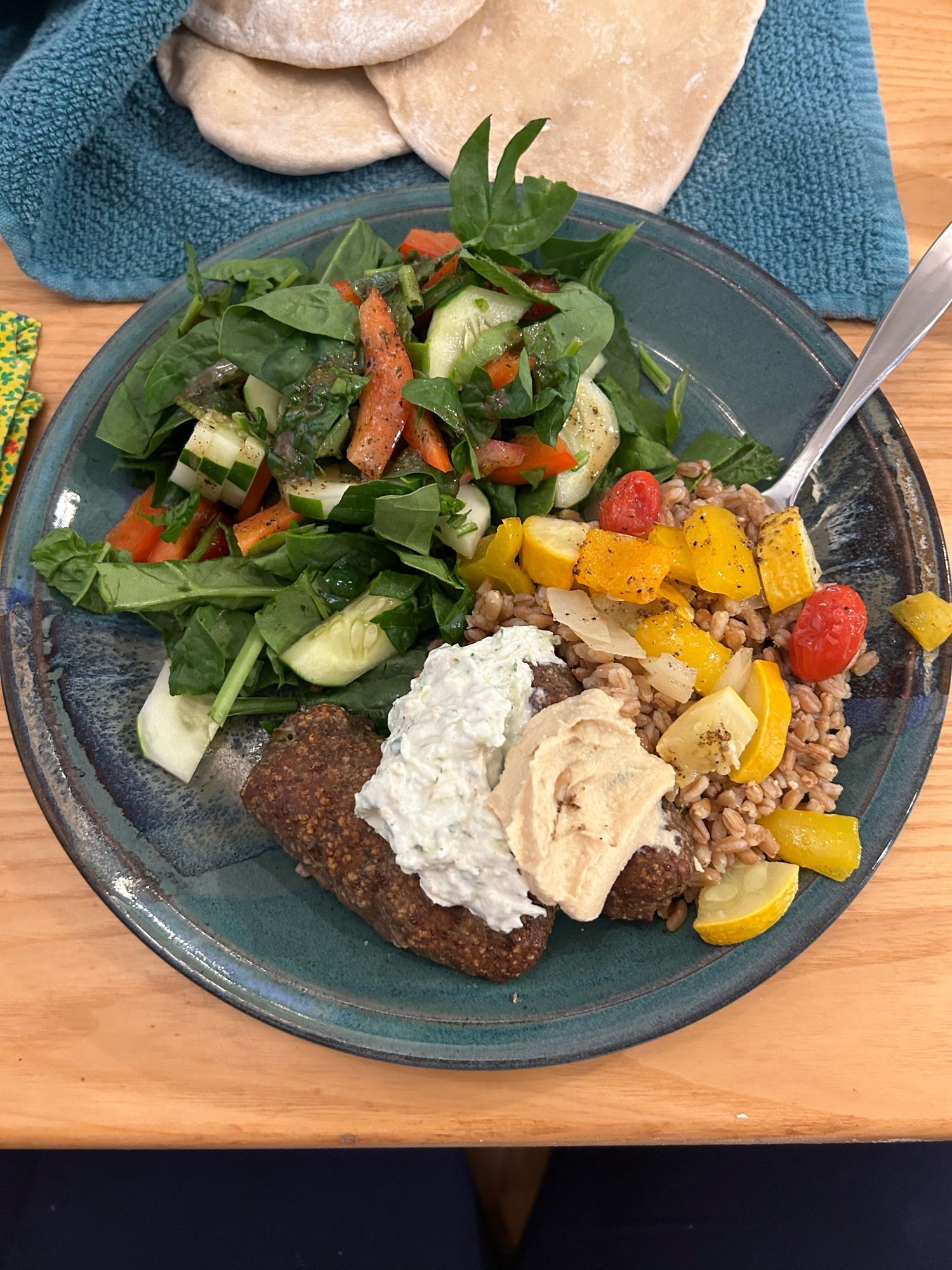 A plate with a salad, farro and roasted veggies, and kebabs covered in sauces