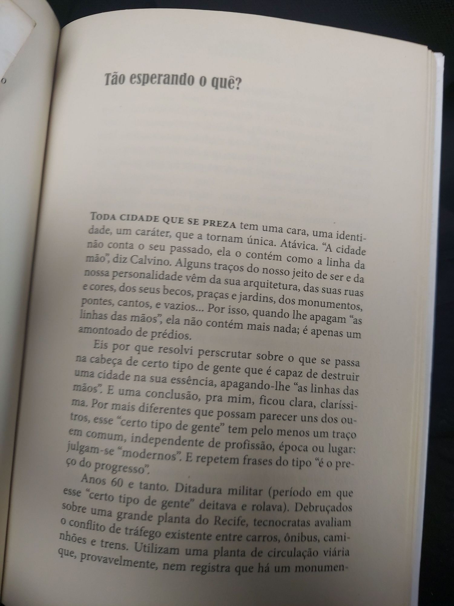 Foto de uma página de um livro, no título está escrito "tão esperando o quê?". Um trecho do texto fala "quando lhe apagam 'as linhas das mãos' ela não contém mais nada, é apenas um amontoado de prédios" em referência às mudanças nos espaços históricos do Recife