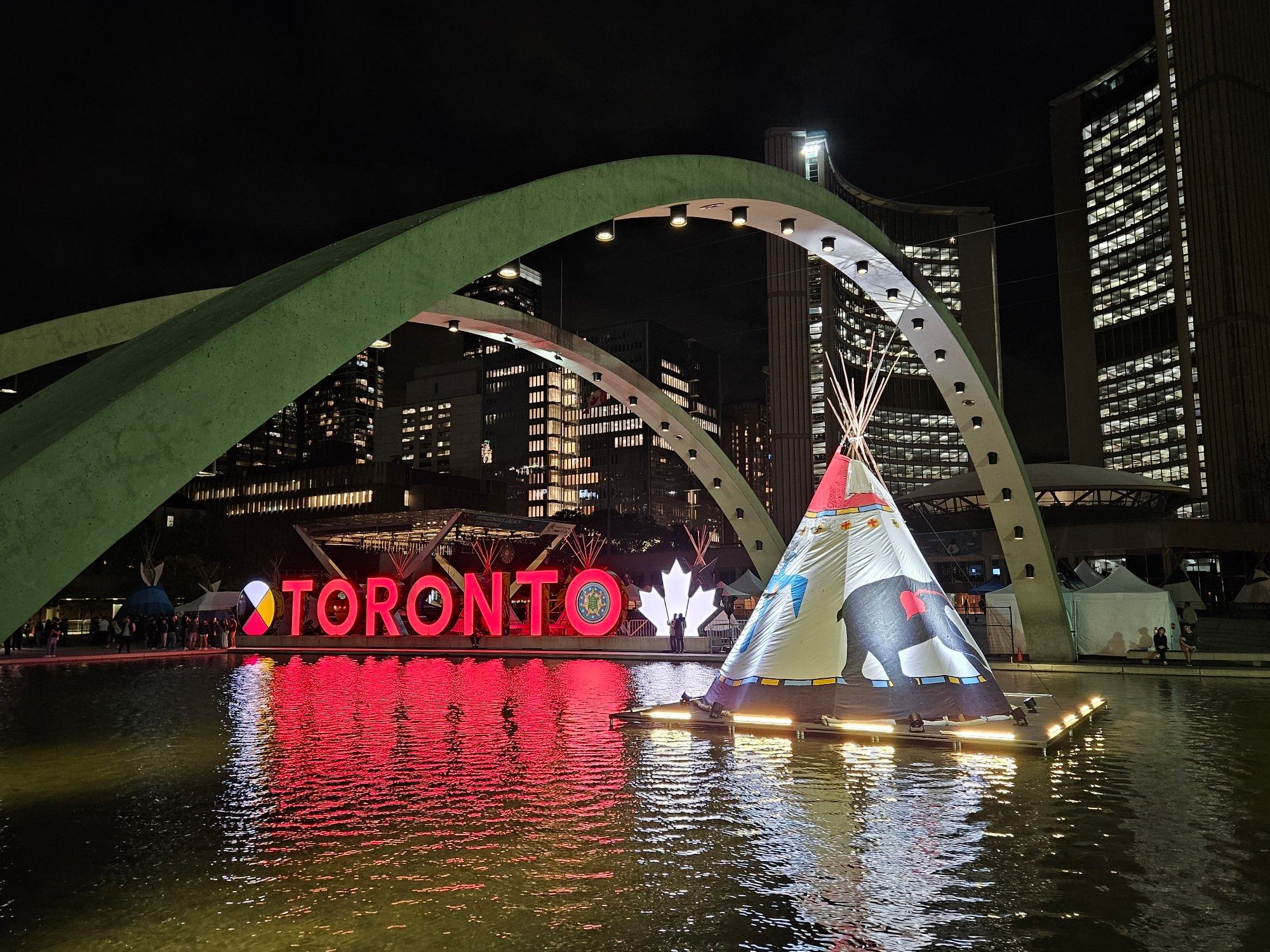 The Toronto sign illuminated at night alongside a lit up teepee.