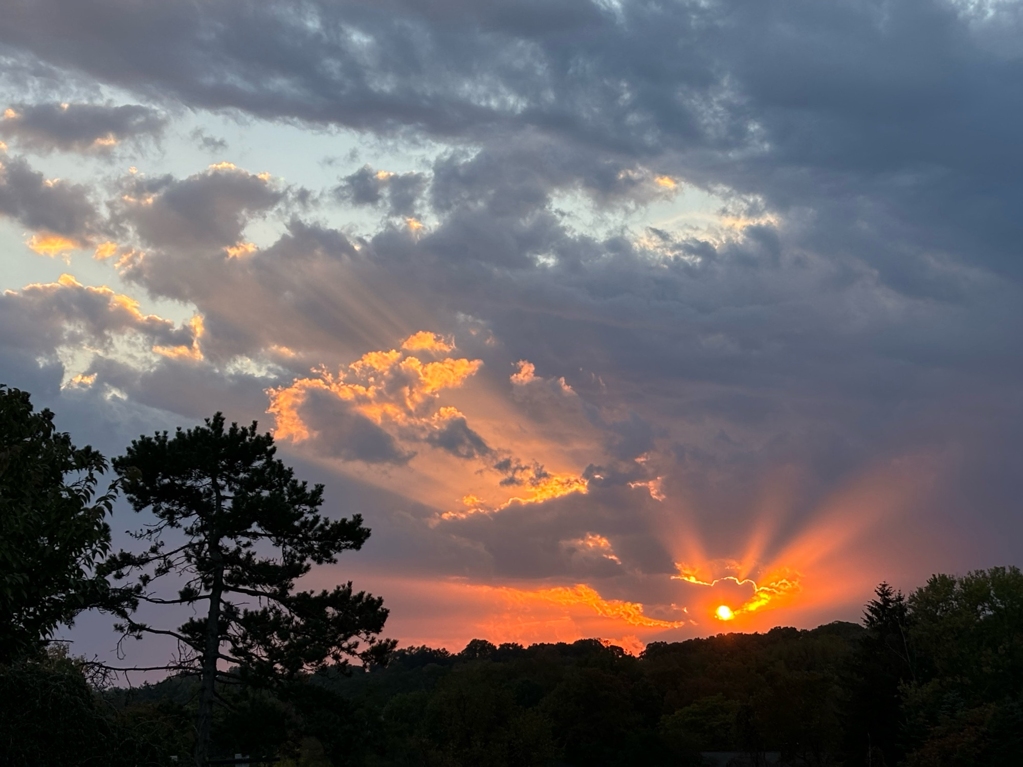 Bright orange sun going down amid dark grey clouds 