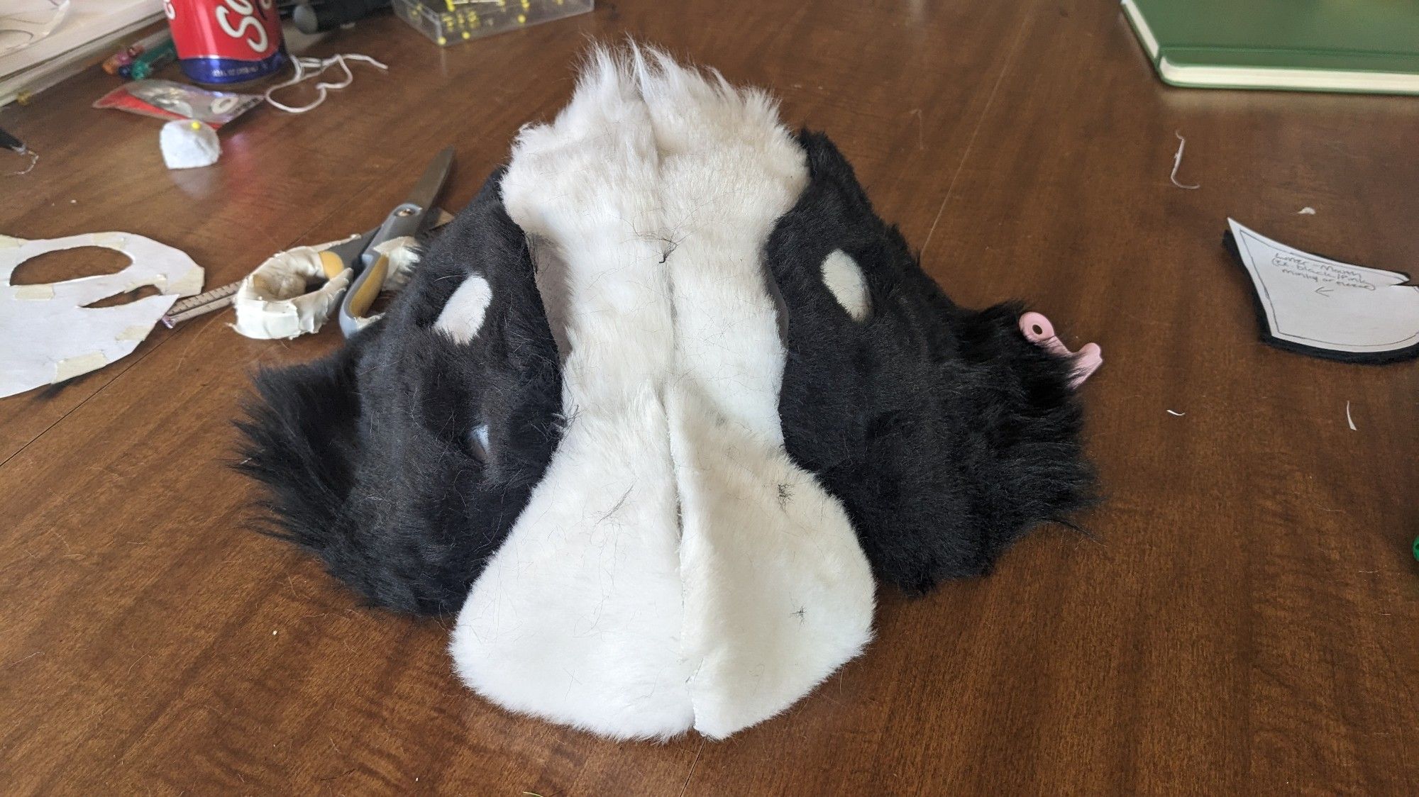 A work in progress half mask on a wooden table with various craft items strewn around. It has black and white fur with classic border collie markings.
#furry #fursuitmaker #therian #maskmaker