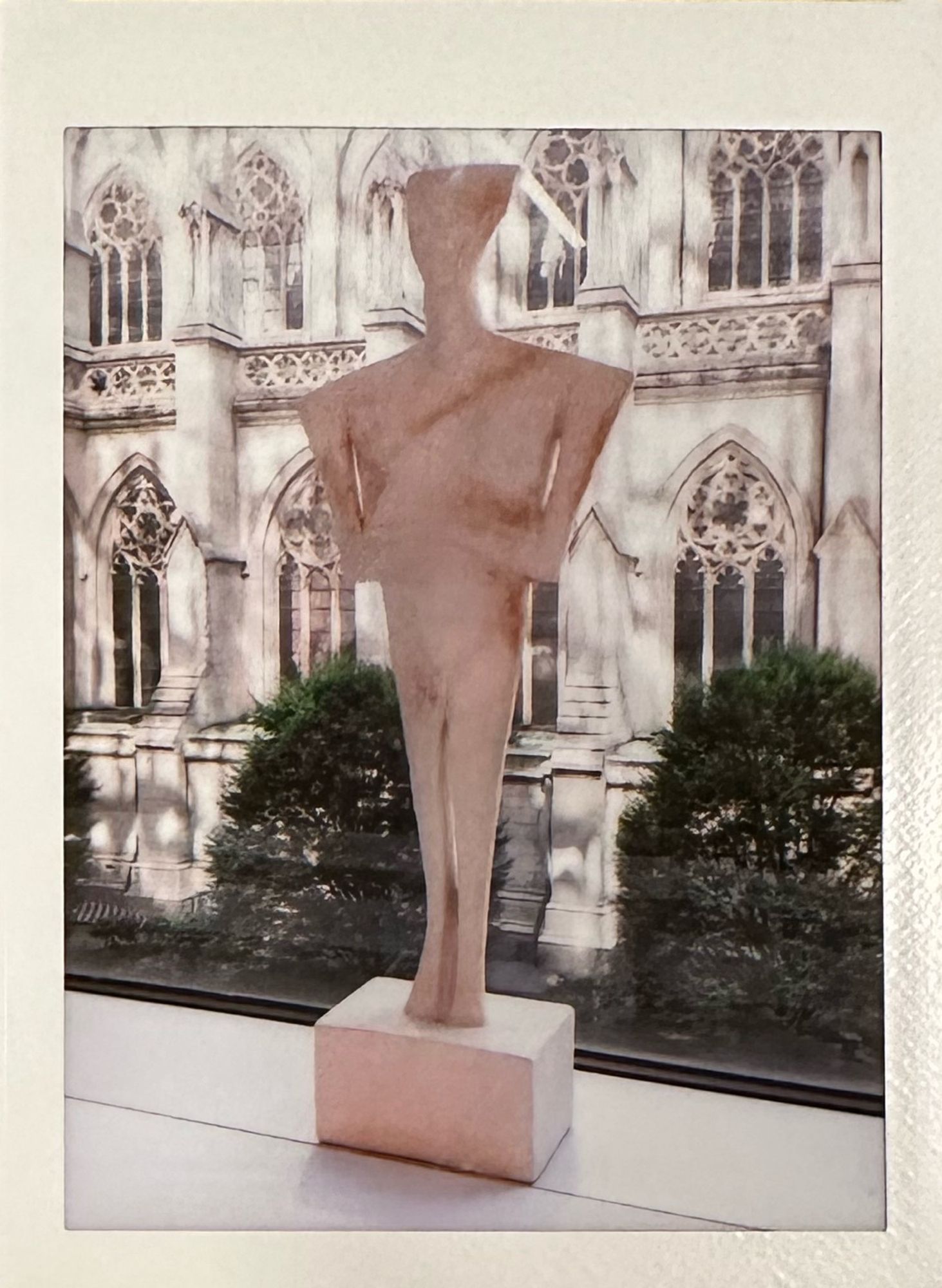 Photo of an Instax print of a statuette on a windowsill with St. Patrick’s Cathedral in the background