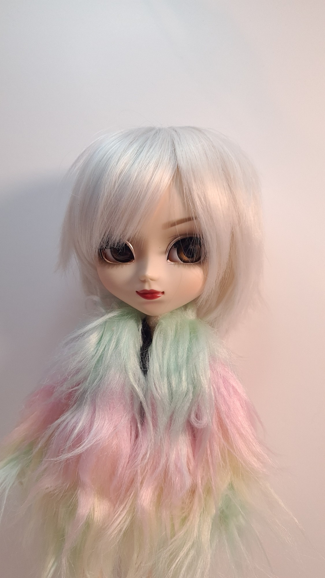 This is a white haired doll wearing a rainbow pastel fur coat.