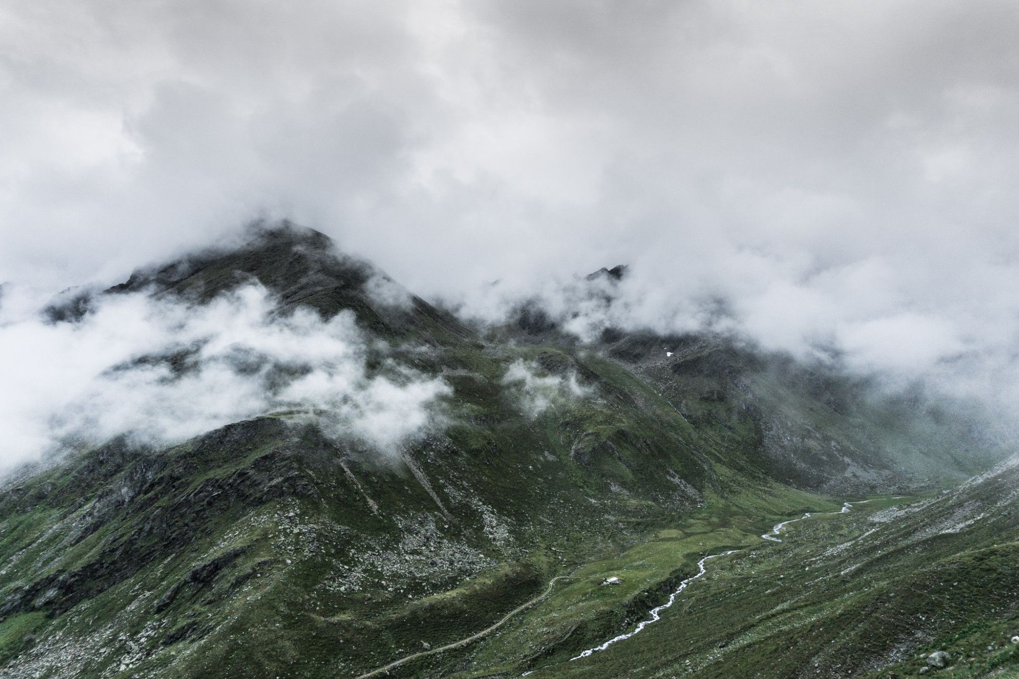 Blick vom Berg in ein grünes, sehr wolkenverhangenes Tal.