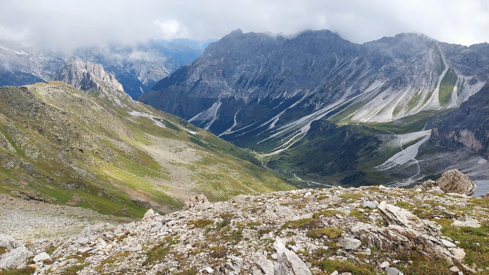 Blick vom Joch ins Tal. Links Wiesenhänge, rechts Felsberge.