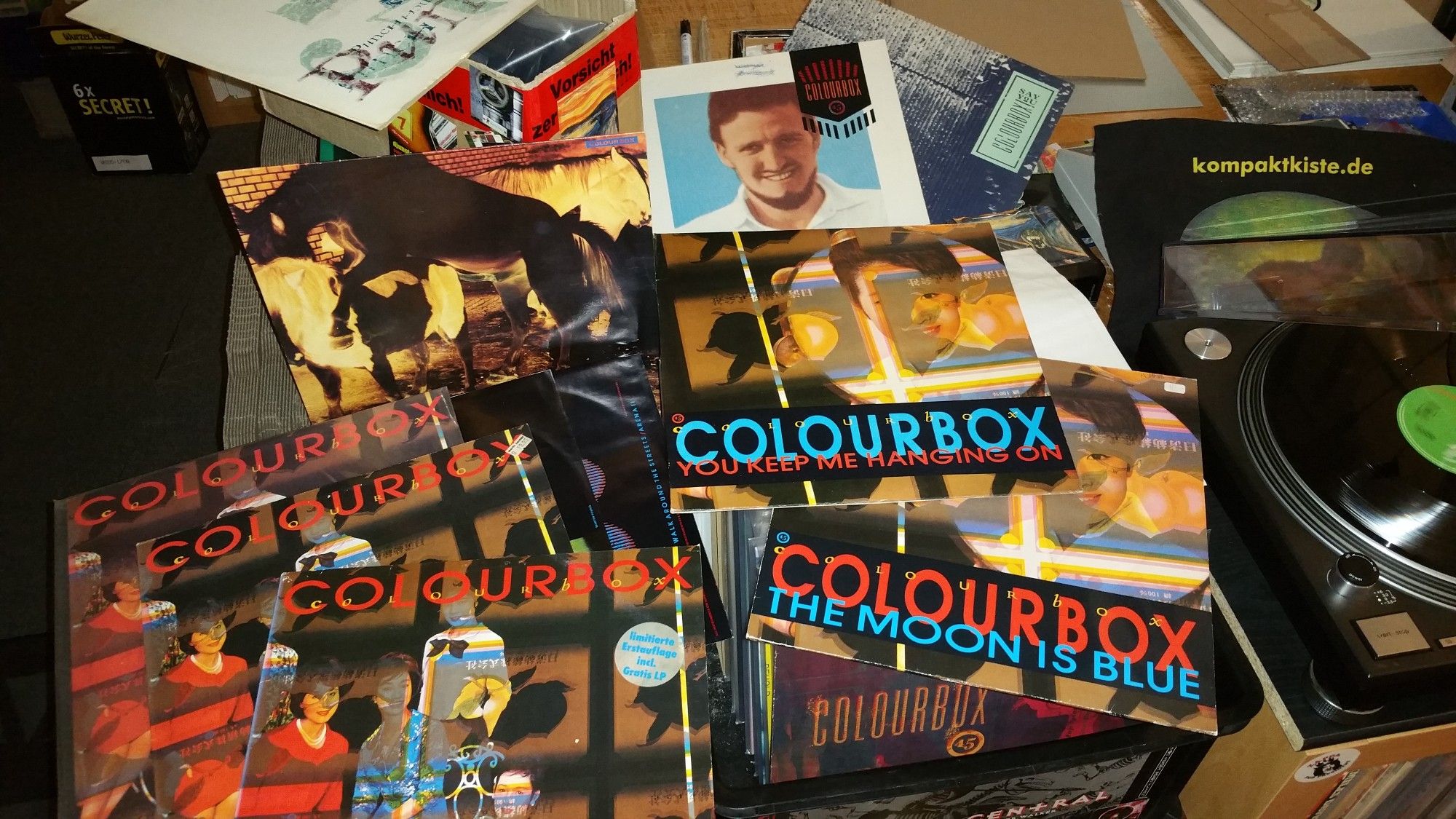 a pile of Colourbox LPs and 12" Singles beside the vinyl record player