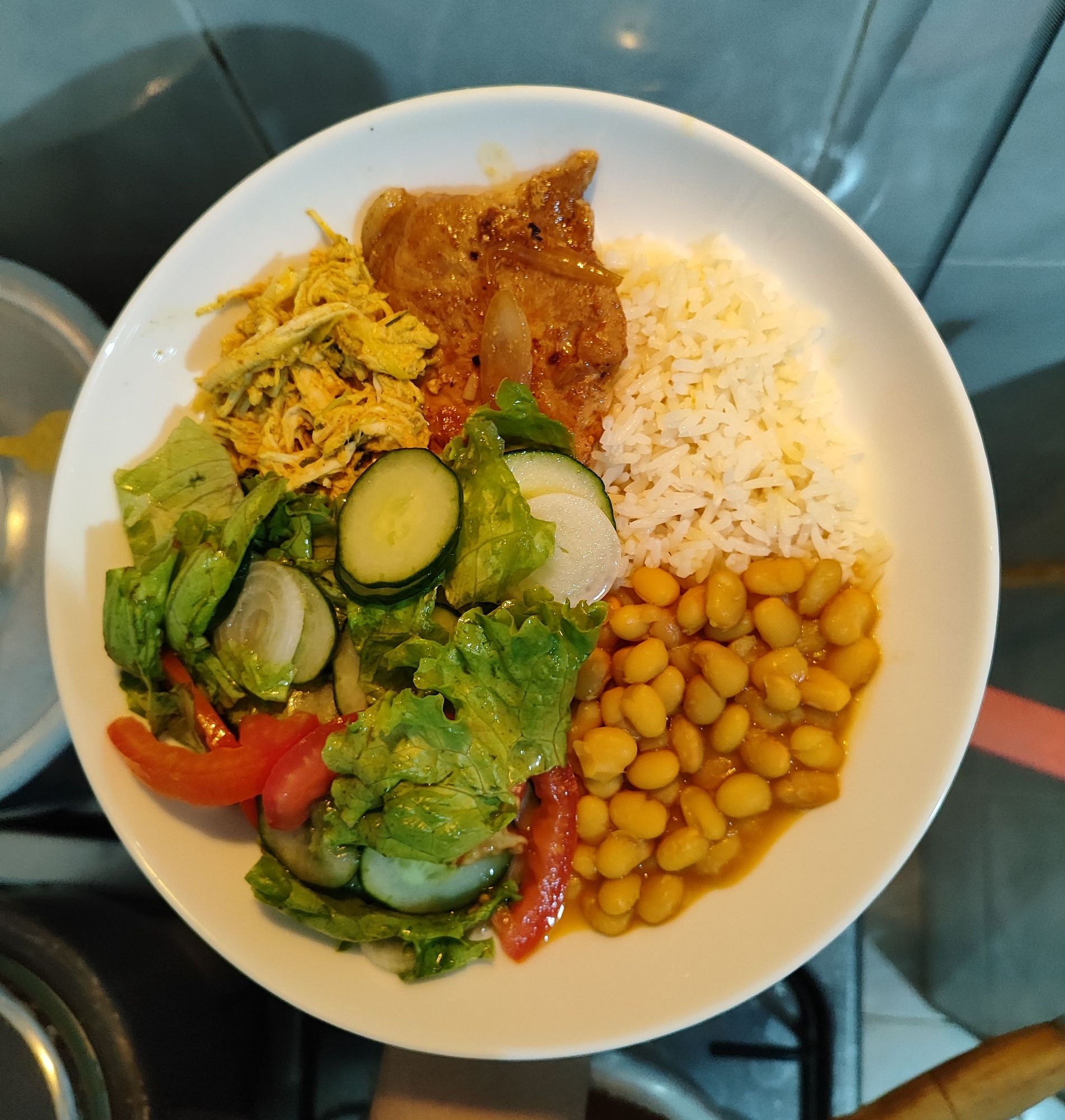 Prato branco com arroz feijão, bisteca suína, frango cozido desfiado e salada de alface, tomate, pepino e cebola.