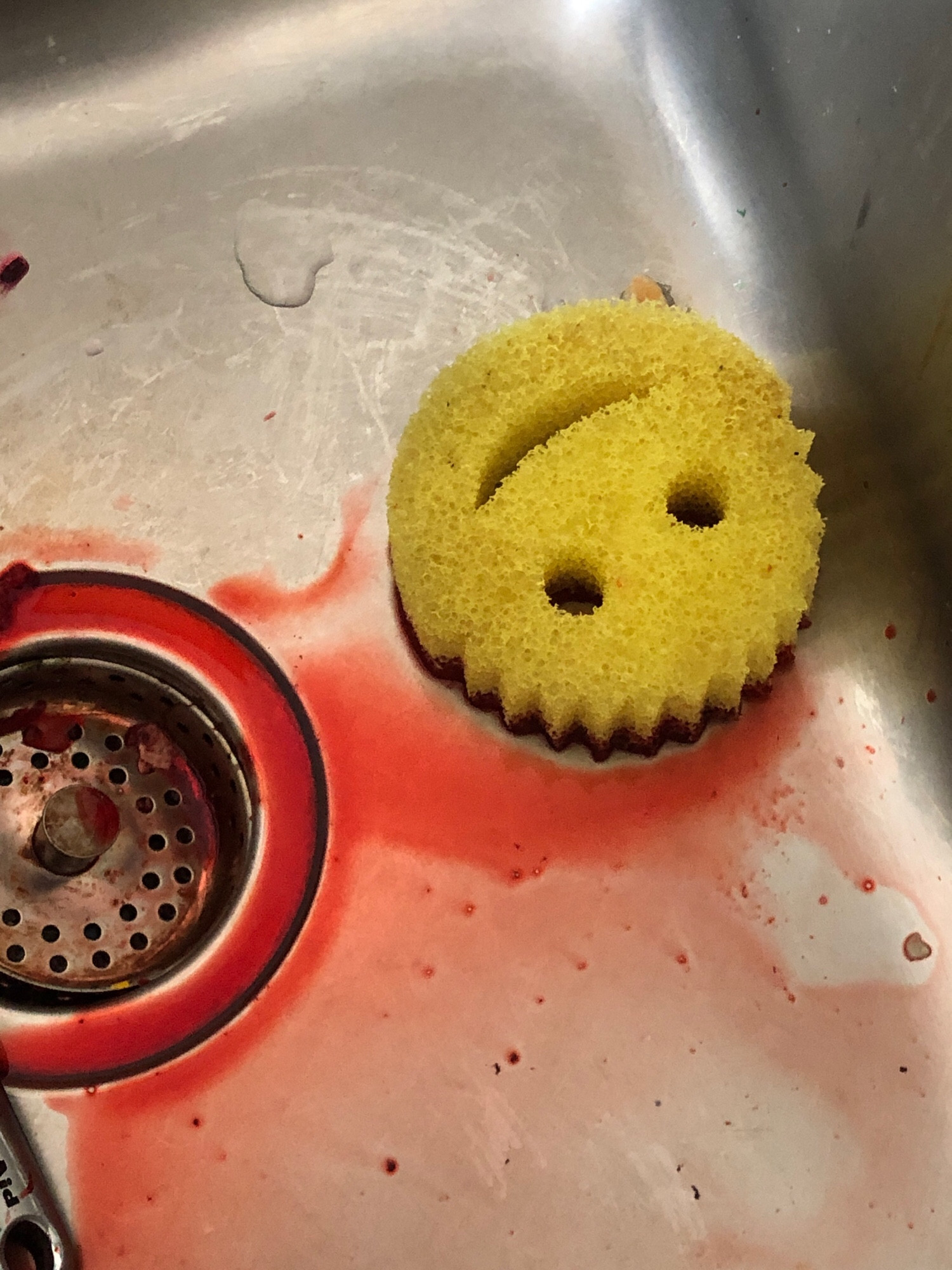 a smiley face scrub daddy sponge in the sink in a puddle of bright red beet juice.