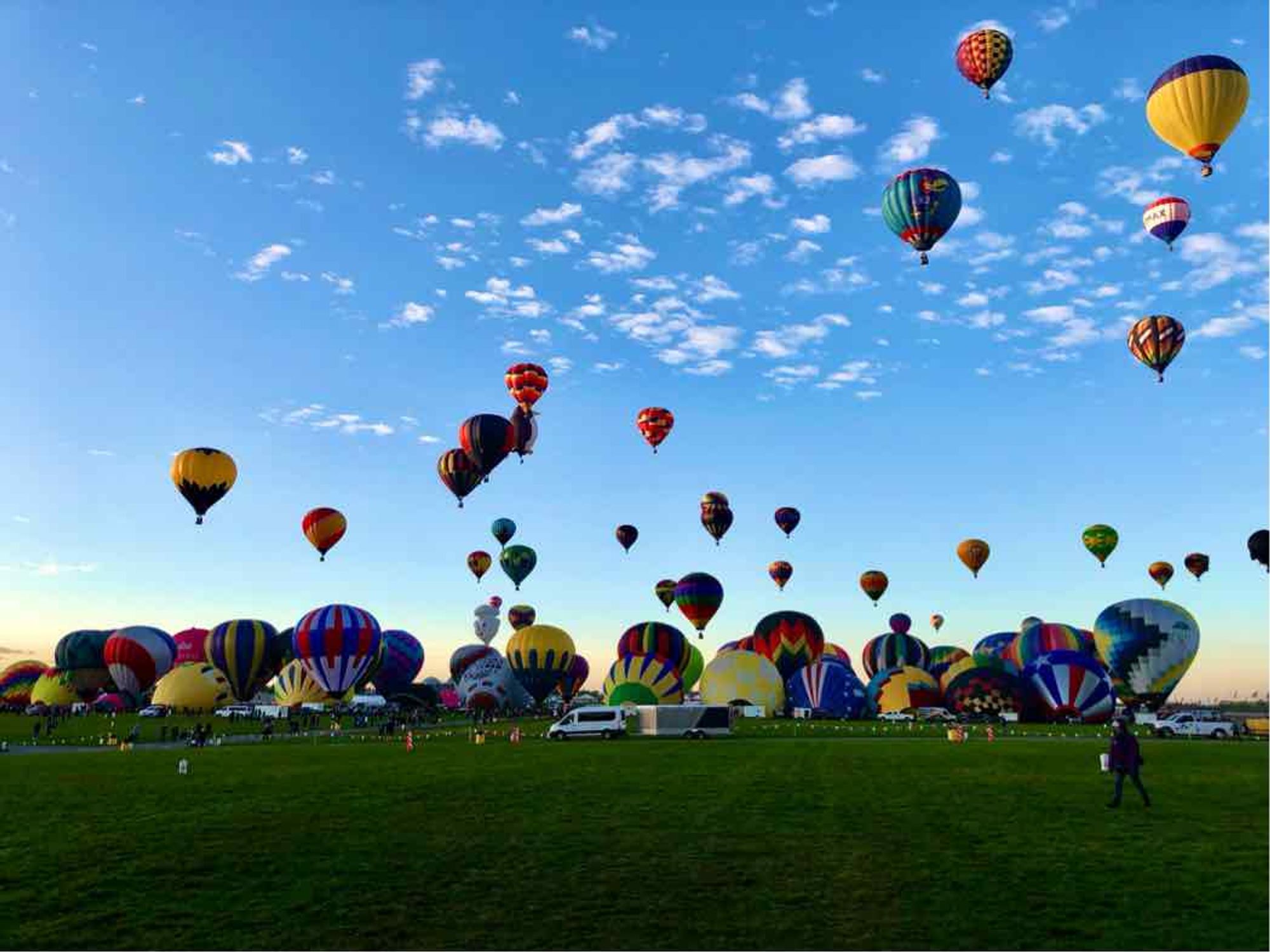 Color photo of Hot Air Balloons preparing for take off with a few in the air.