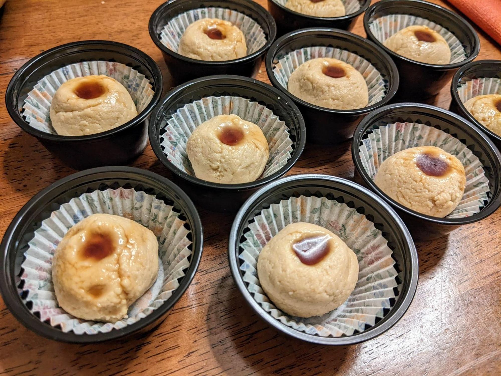 Balls of sandesh in paper cups inside condiment cups and with each ball with a bit of the gur in a small depression in the top of the sandesh