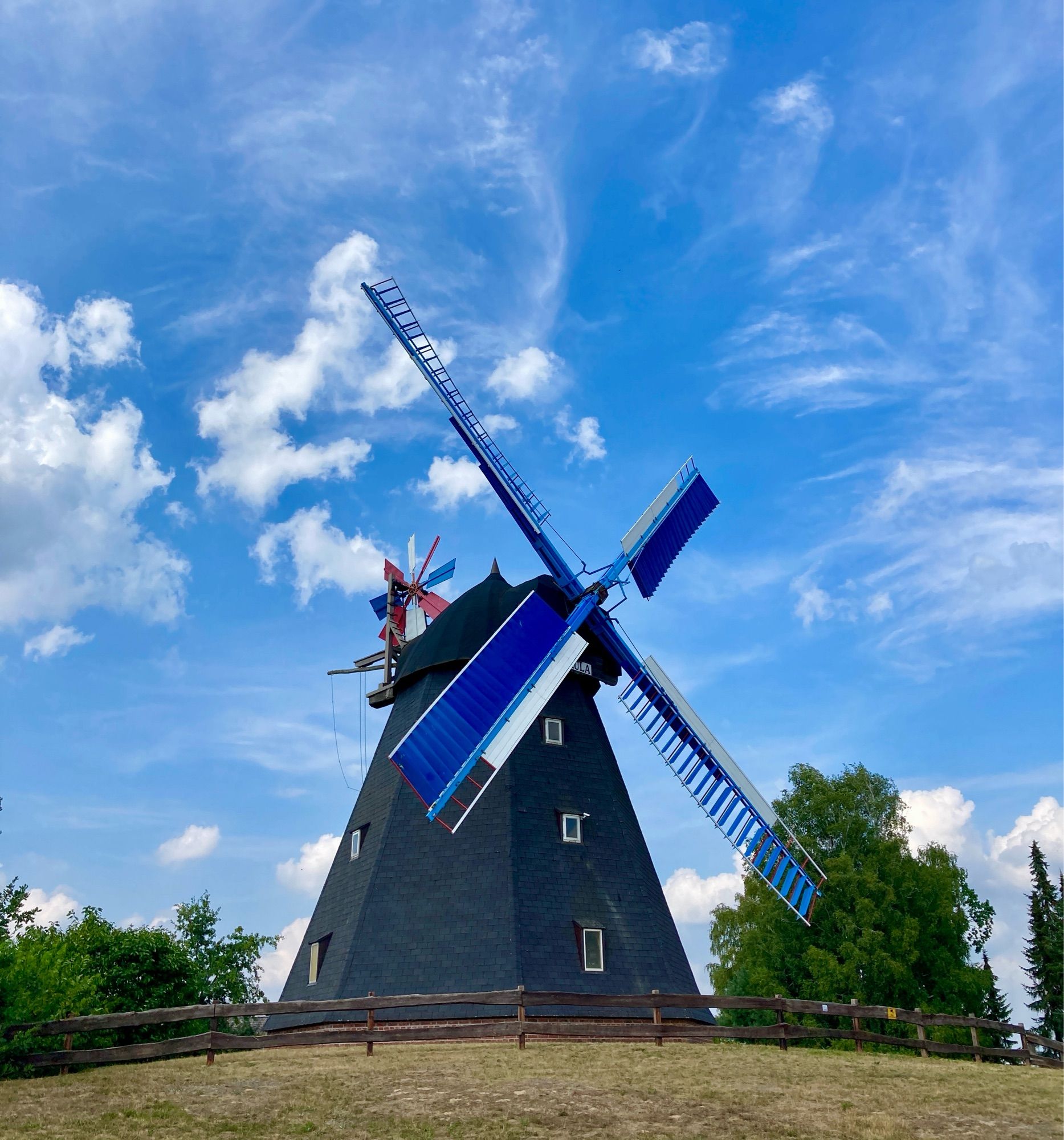 Windmühle auf einen kleinen Hügel, daneben stehen Bäume , Wolkenhimmel