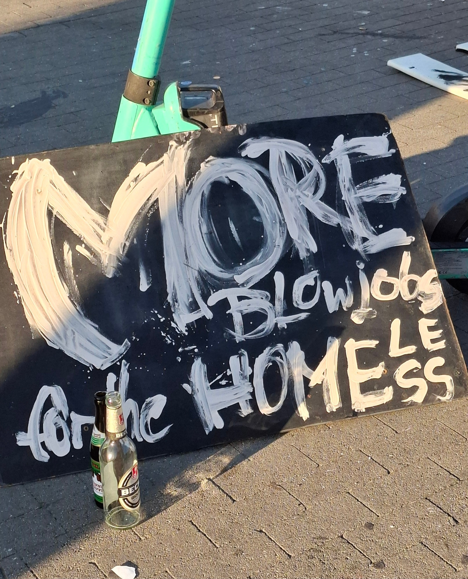 a hand painted sign displayed by a homeless artist that says "more blowjobs for the homeless"