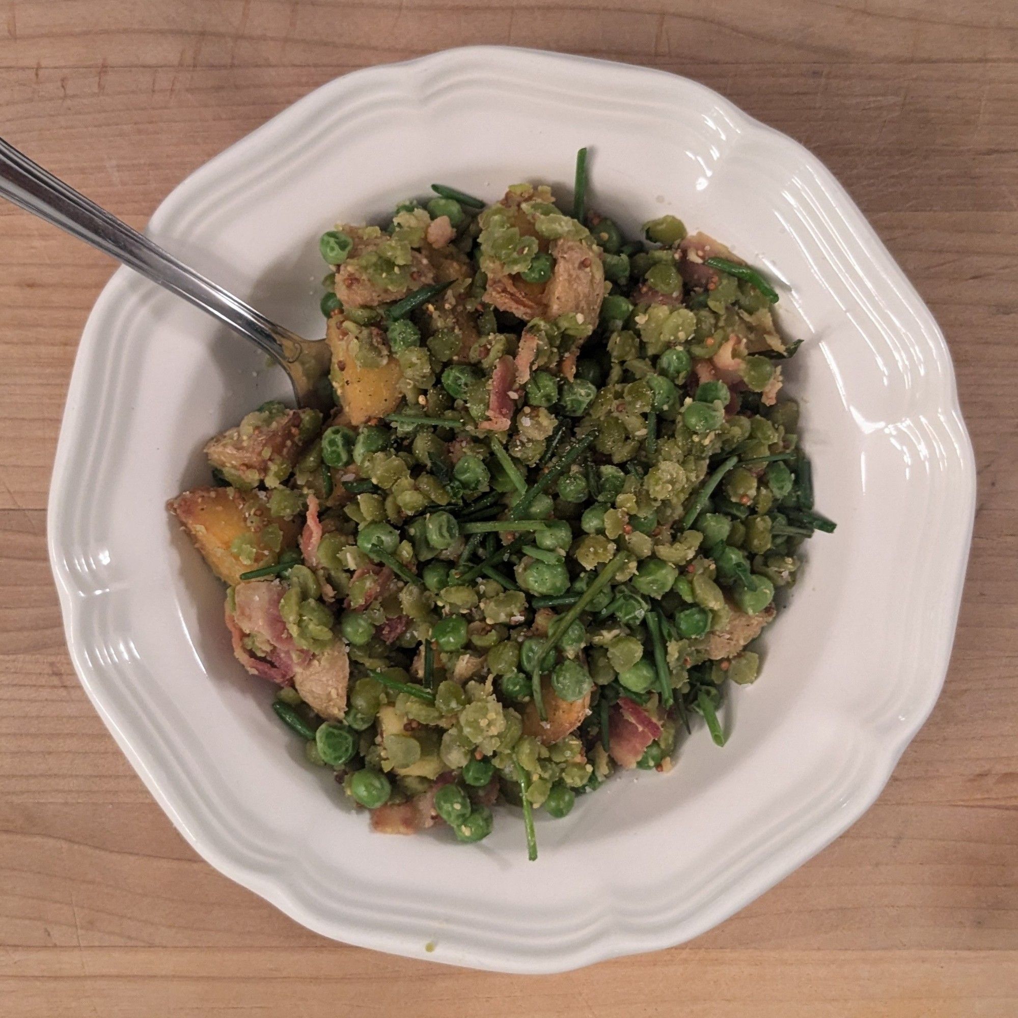 a white bowl with browned potatoes, round green peas, red bacon bits, and green chives