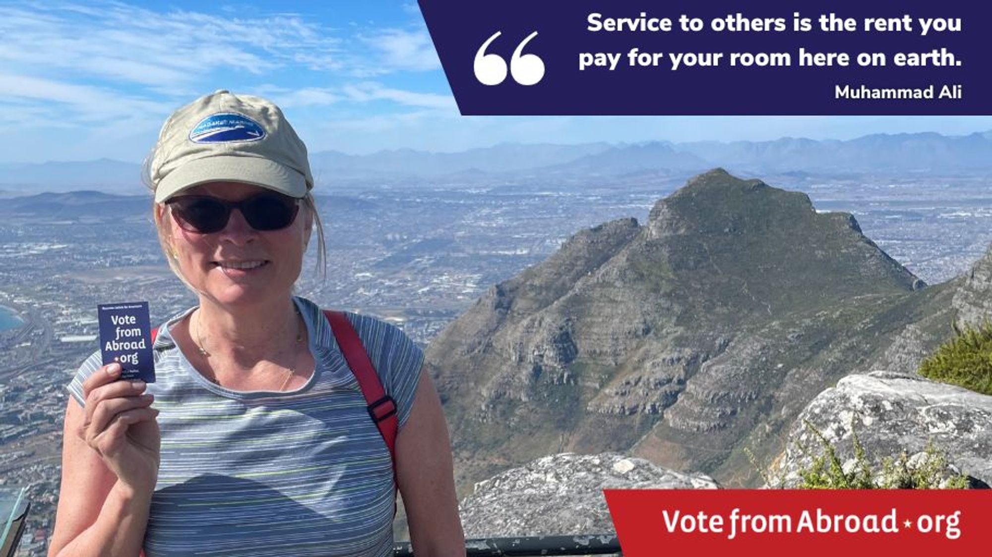 A woman wearing a baseball cap and a blue Tshirt is standing in front of a mountain vista, and she is holding a card that says "VoteFromAbroad.org." There is a blue block on the top right saying "Service to others is the rent you pay for your room here on earth. from Muhammad Ali" and a VoteFromAbroad.org logo is in the lower left corner. 