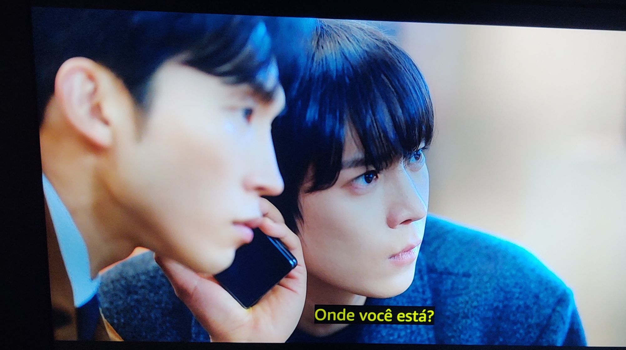 A foto é de dois personagens da série No gain no love, Ji-uk e Gyu Hyun, um está falando ao telefone e o outro colado ouvindo a conversa