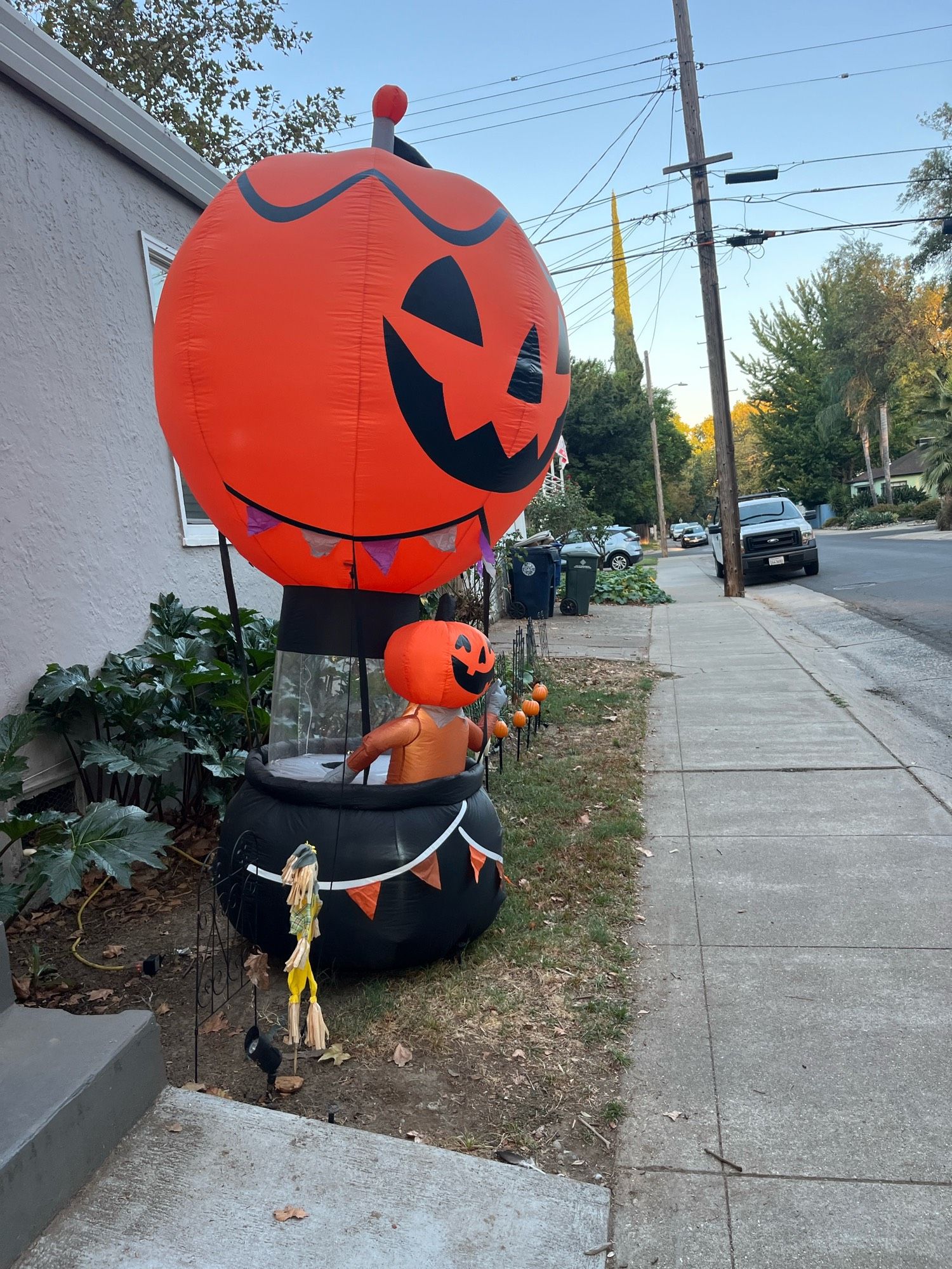 A lawn Halloween decoration that appears to be a man with a jack o lantern head riding in a hot air balloon that is also shaped like a jack o lantern.