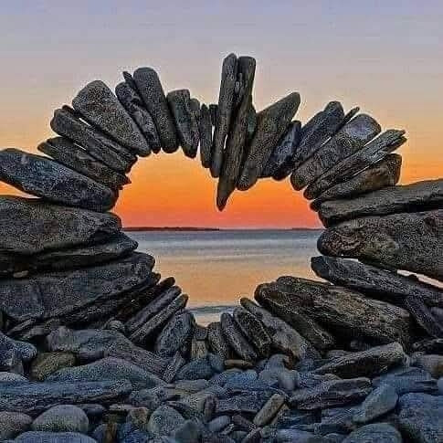 Stones stacked to create a "heart" arch with the beach and sunset behind