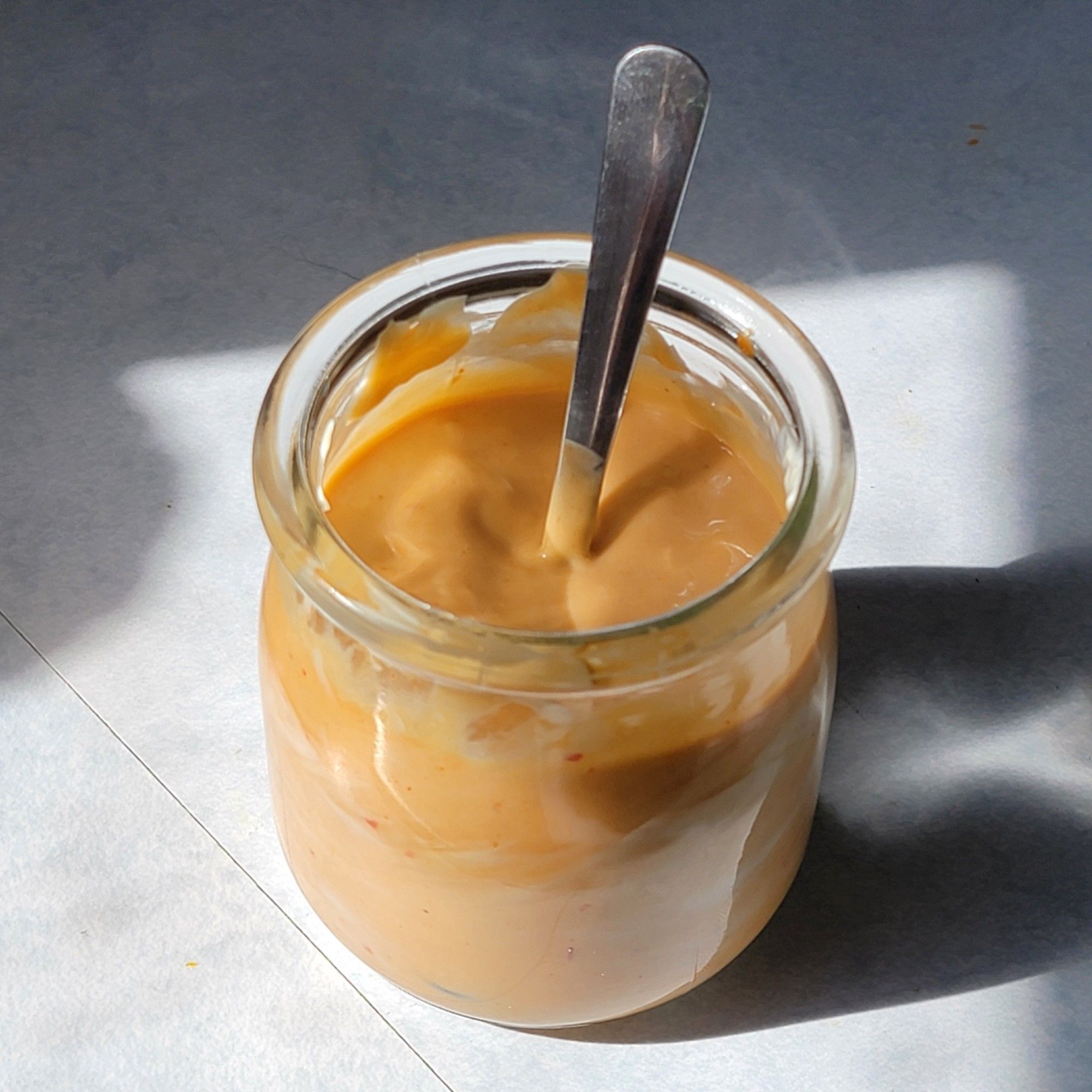 Small jar of a light orange/beige mayo in the sunlight from a window.