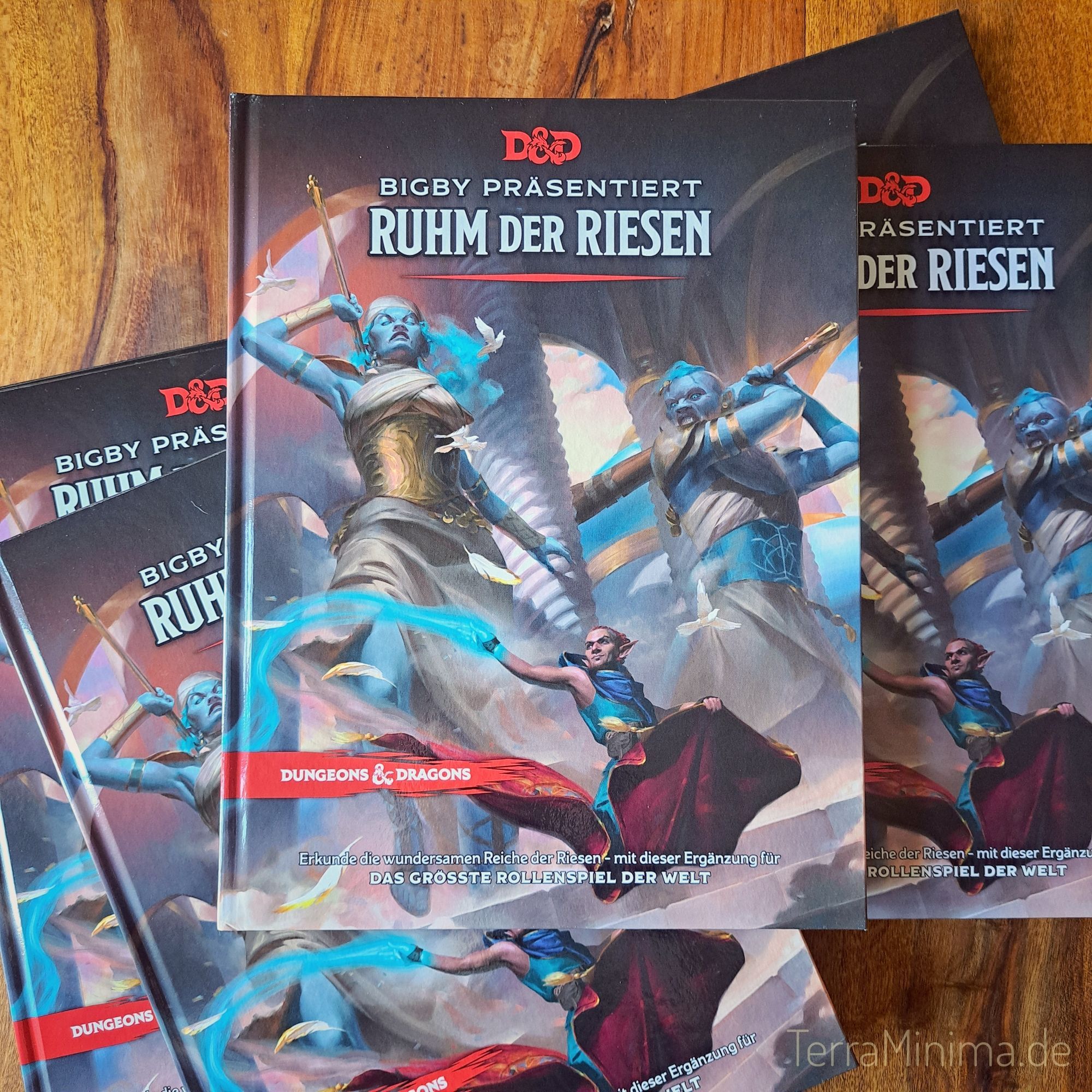 Auf einem Holztisch liegen mehrere gleiche Bücher übereinander mit dem Titel Bigby präsentiert: Ruhm der Riesen