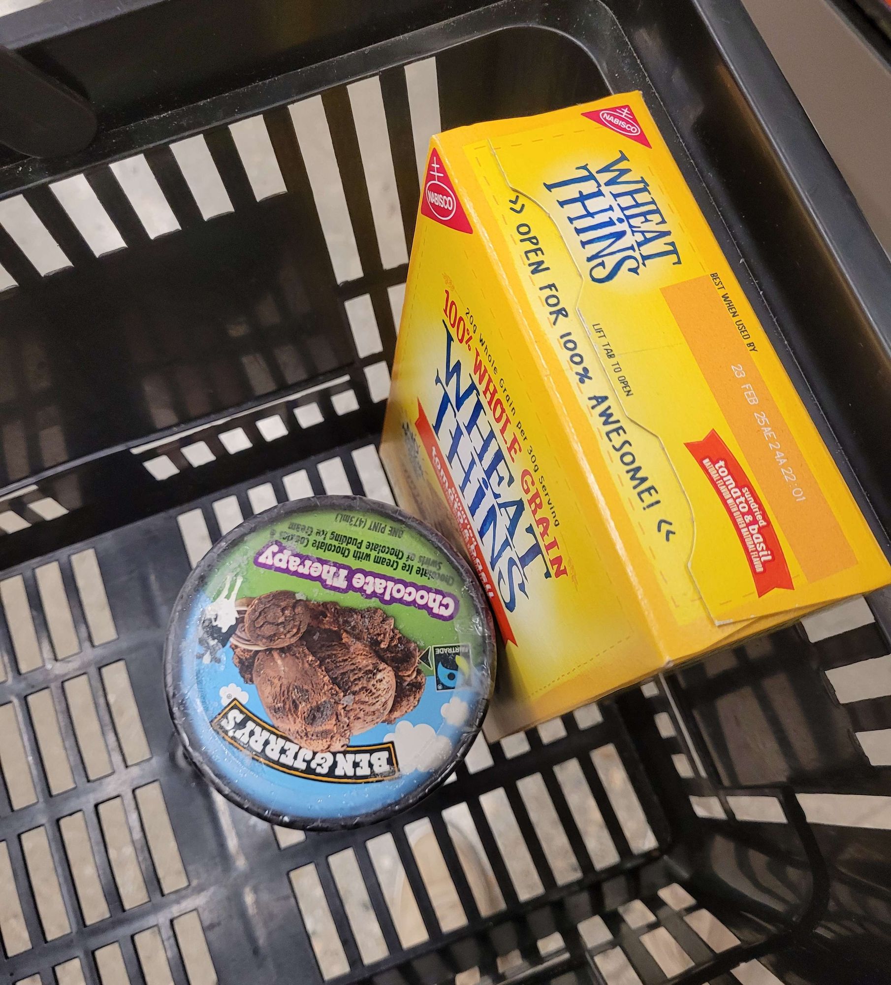 An overhead view looks down into a grocery basket with a box of Wheat Thins and a pint of Ben & Jerry's Chocolate Therapy.