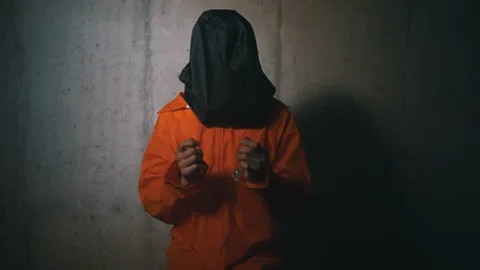 A prisoner in orange jumpsuit with a black bag over their head