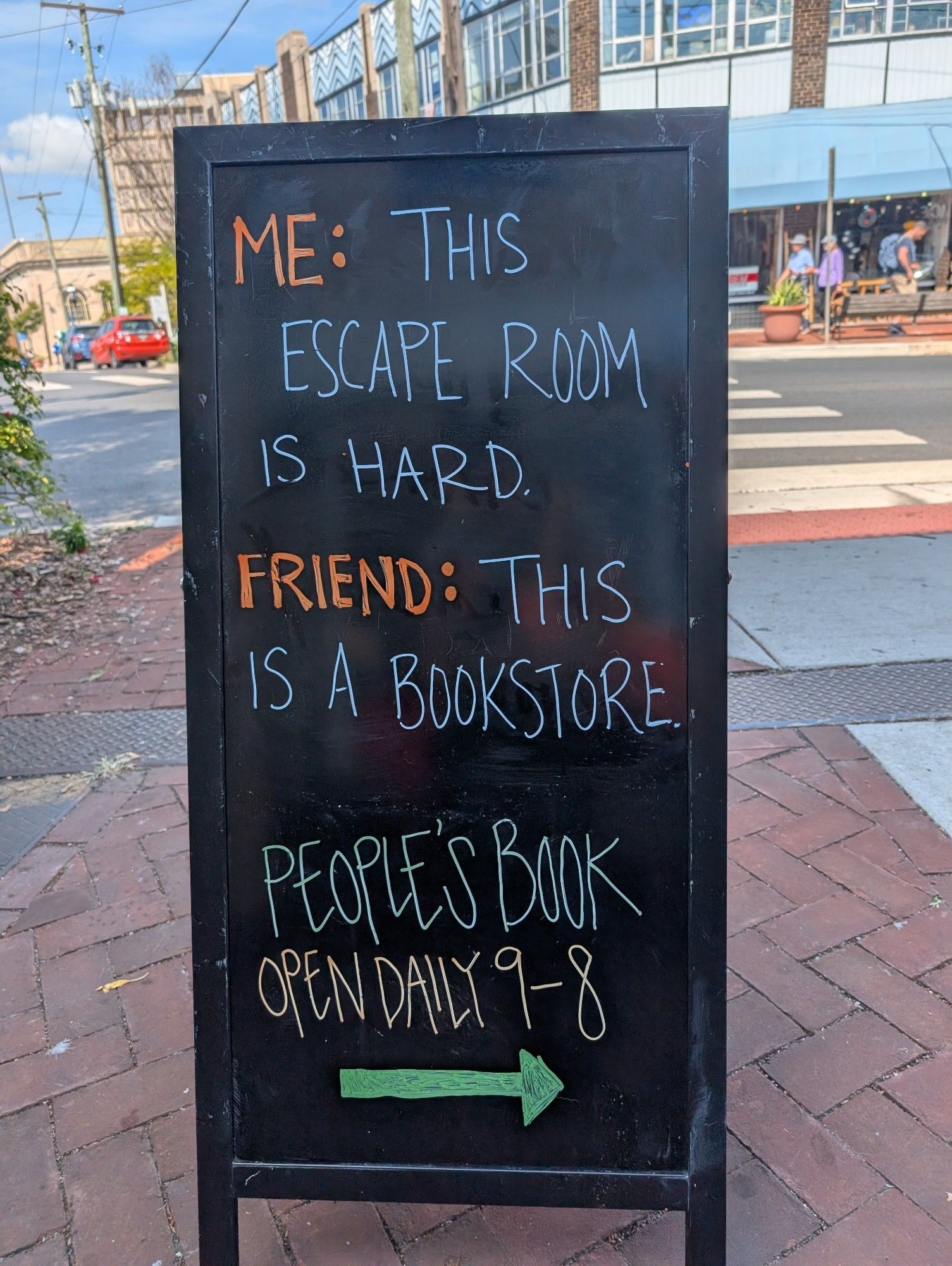 Chalkboard sign reading "Me: This escape room is hard. Friend: This is a bookstore" with an arrow pointing to a bookstore